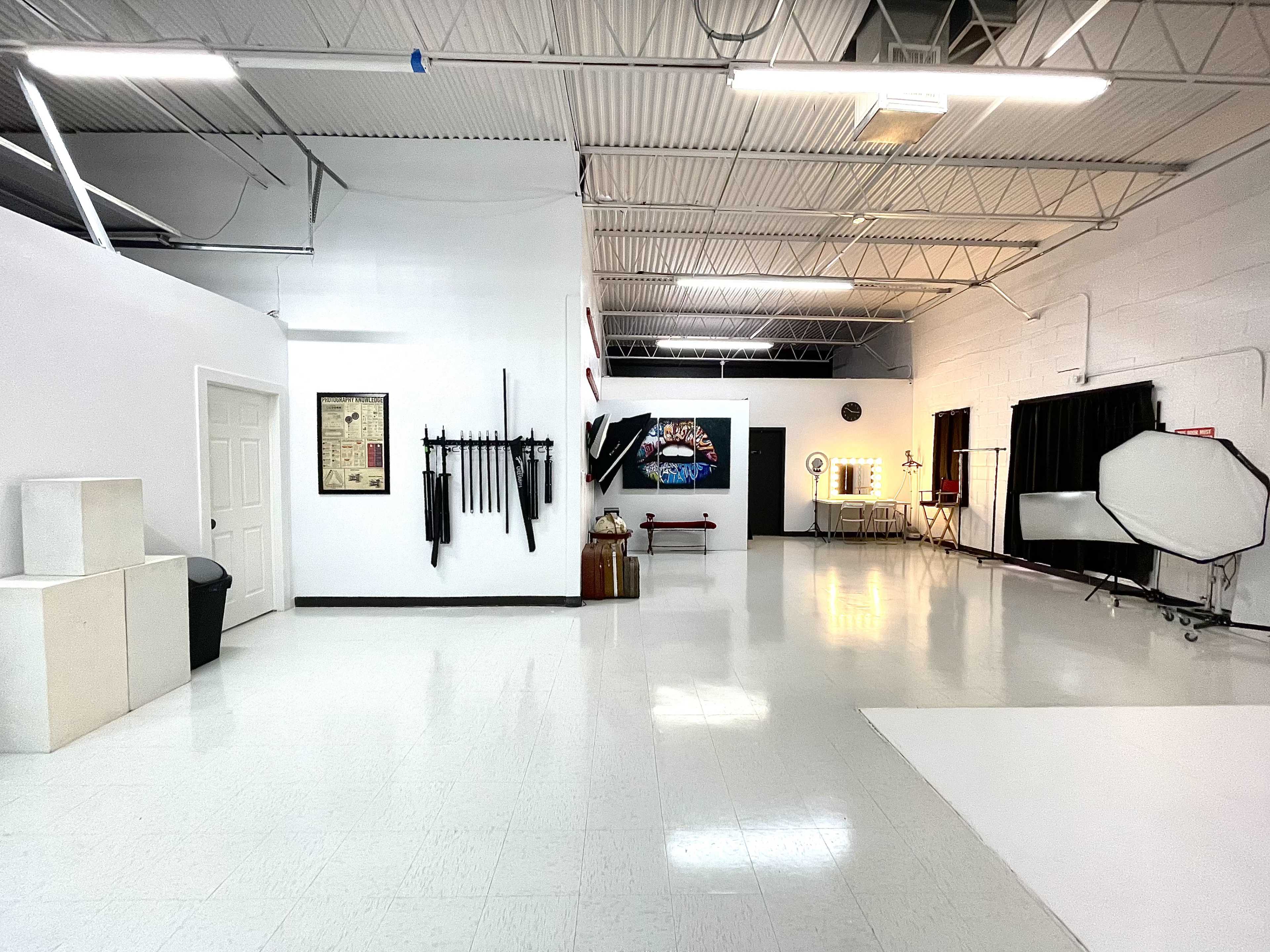 A spacious, well-lit studio with white walls, a clean floor, and various props arranged along one side.