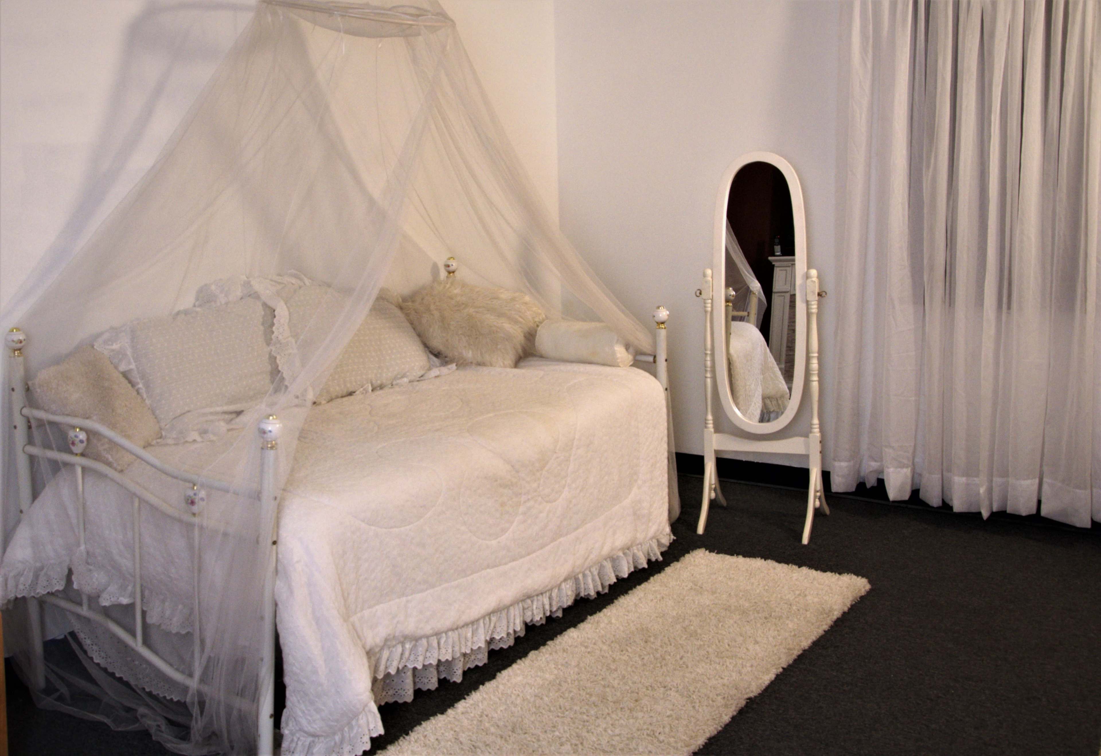 A bedroom with a canopied daybed draped in light fabric next to a full-length mirror and a soft rug on the floor.