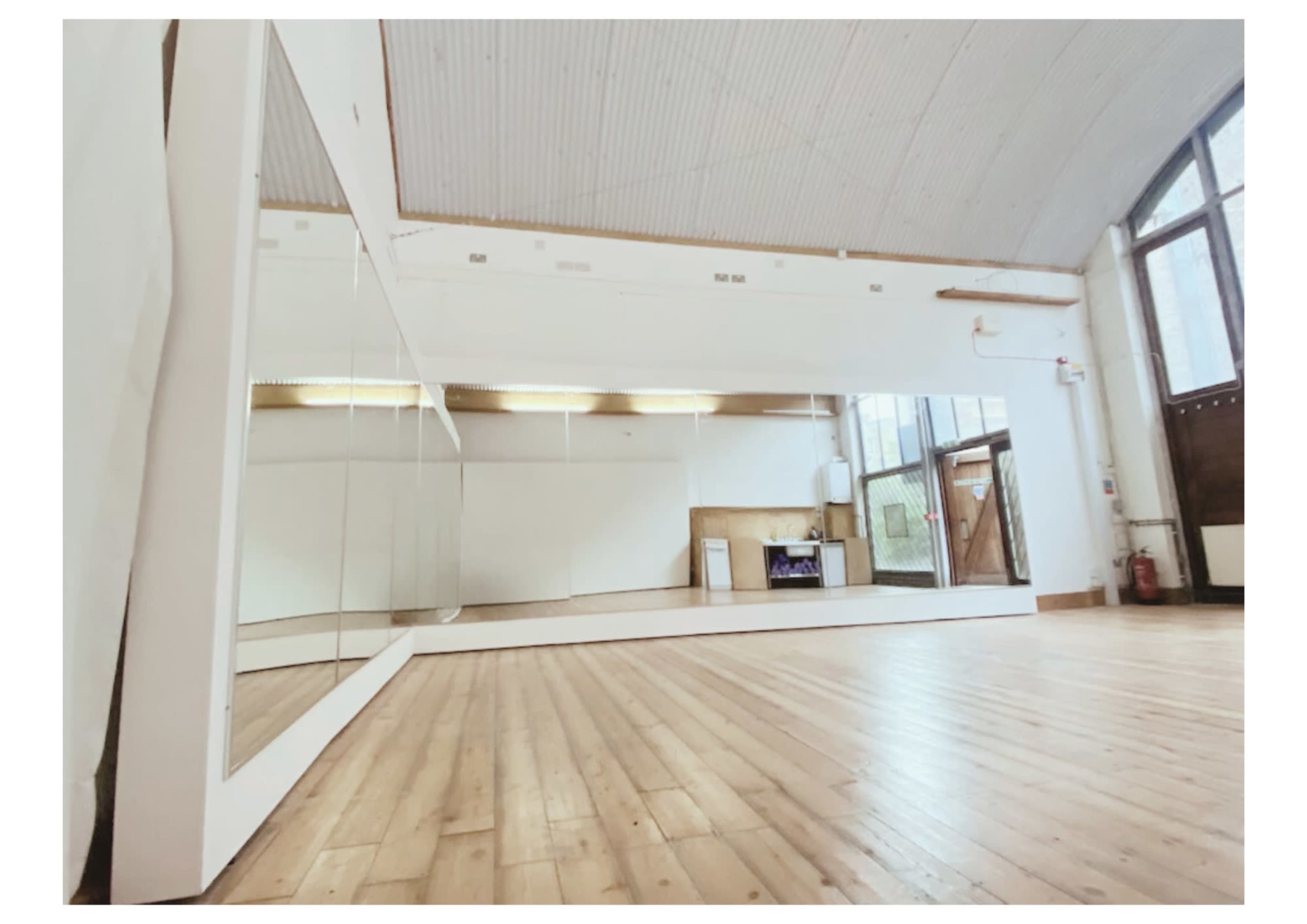 A spacious room with wooden flooring, large mirrors on one wall, and a bright, open atmosphere.