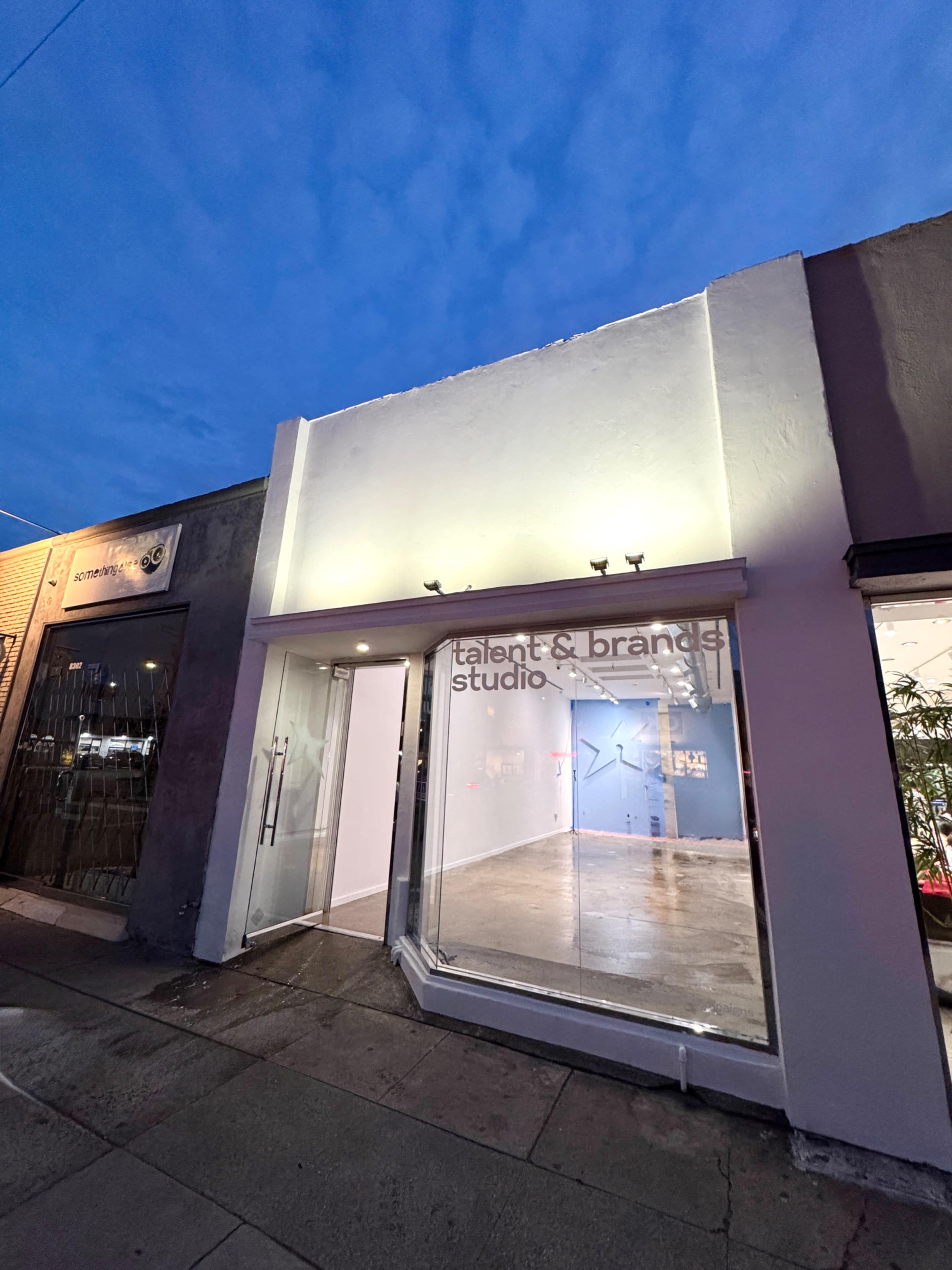 The image shows a modern storefront with a glass front labeled "talent & brand studio" under a twilight sky.