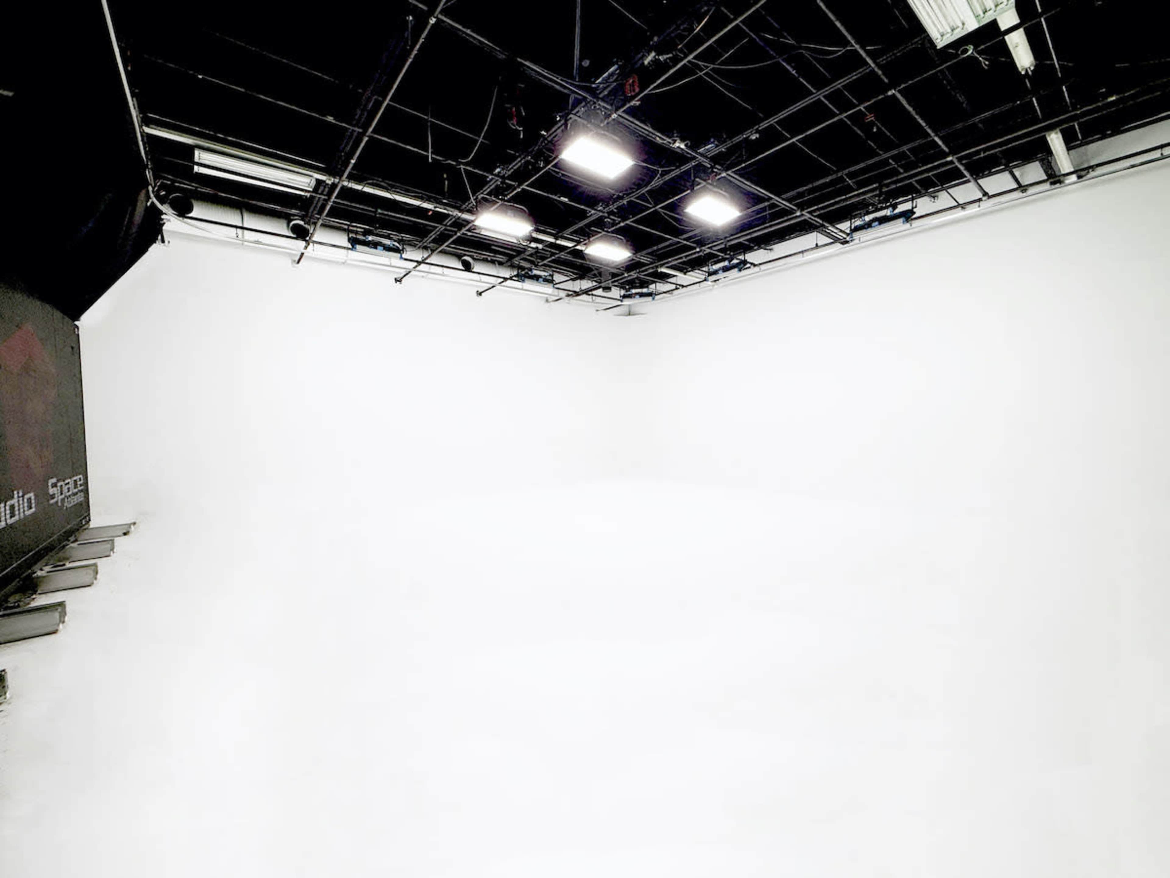 The image shows a large empty studio space with white walls and a grid of overhead lights.