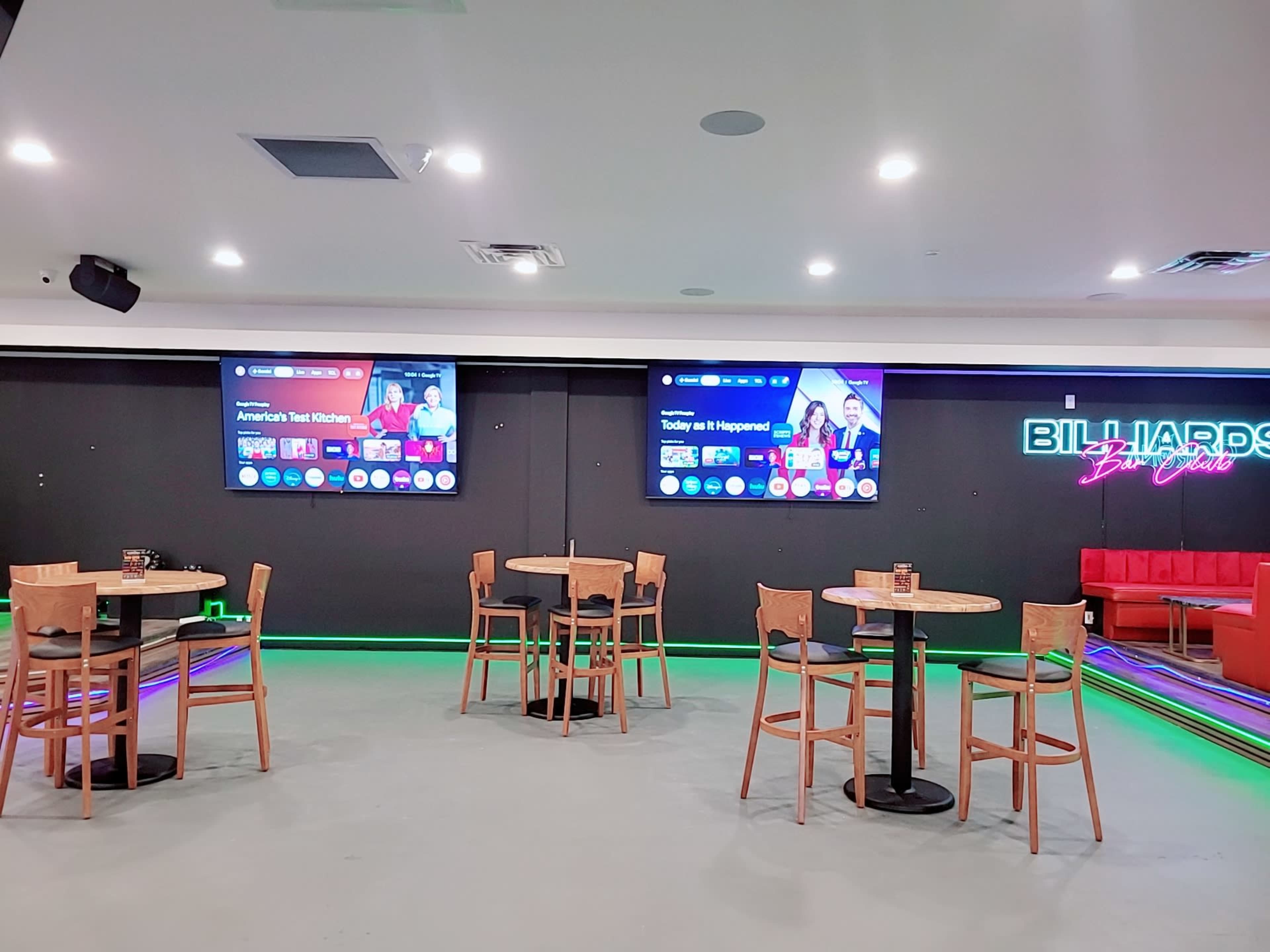 The image shows a modern billiards room with tables and several large screens displaying sports content on the walls.