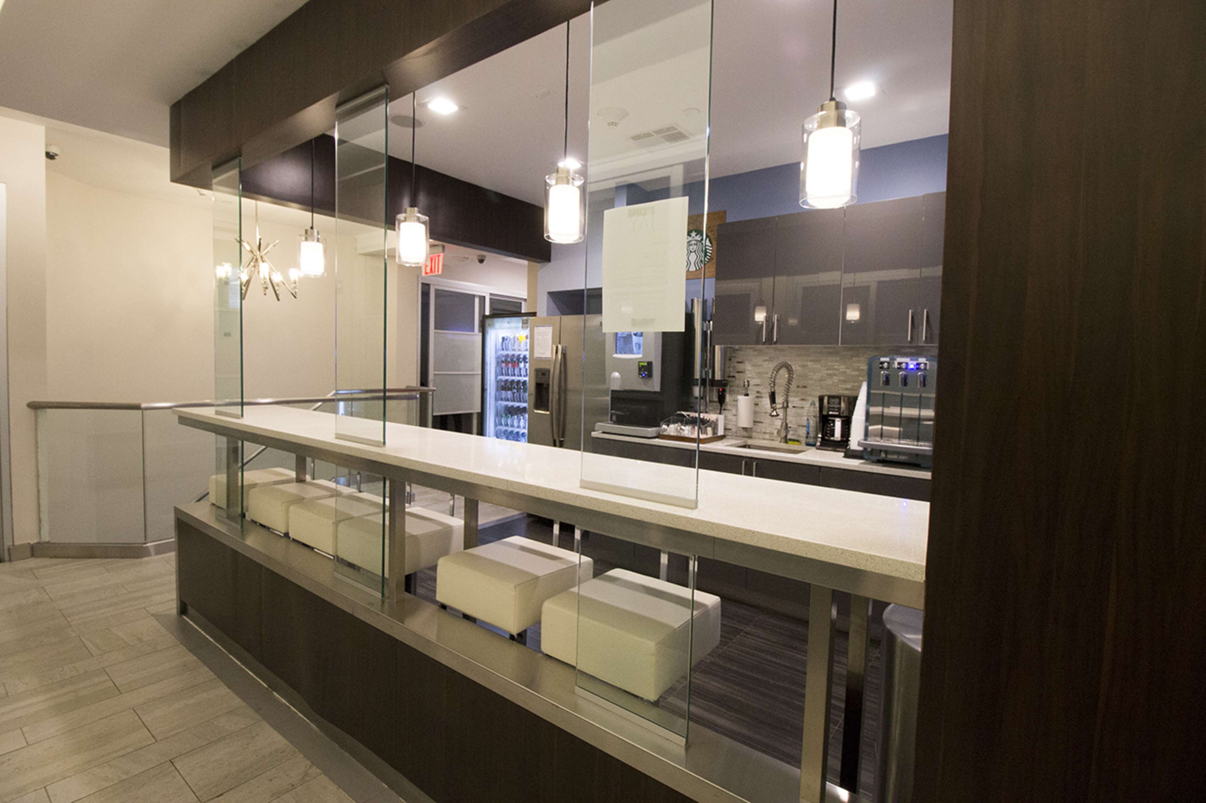 The image shows a modern kitchen or café area featuring a countertop with seating, glass partitions, and stainless steel appliances.