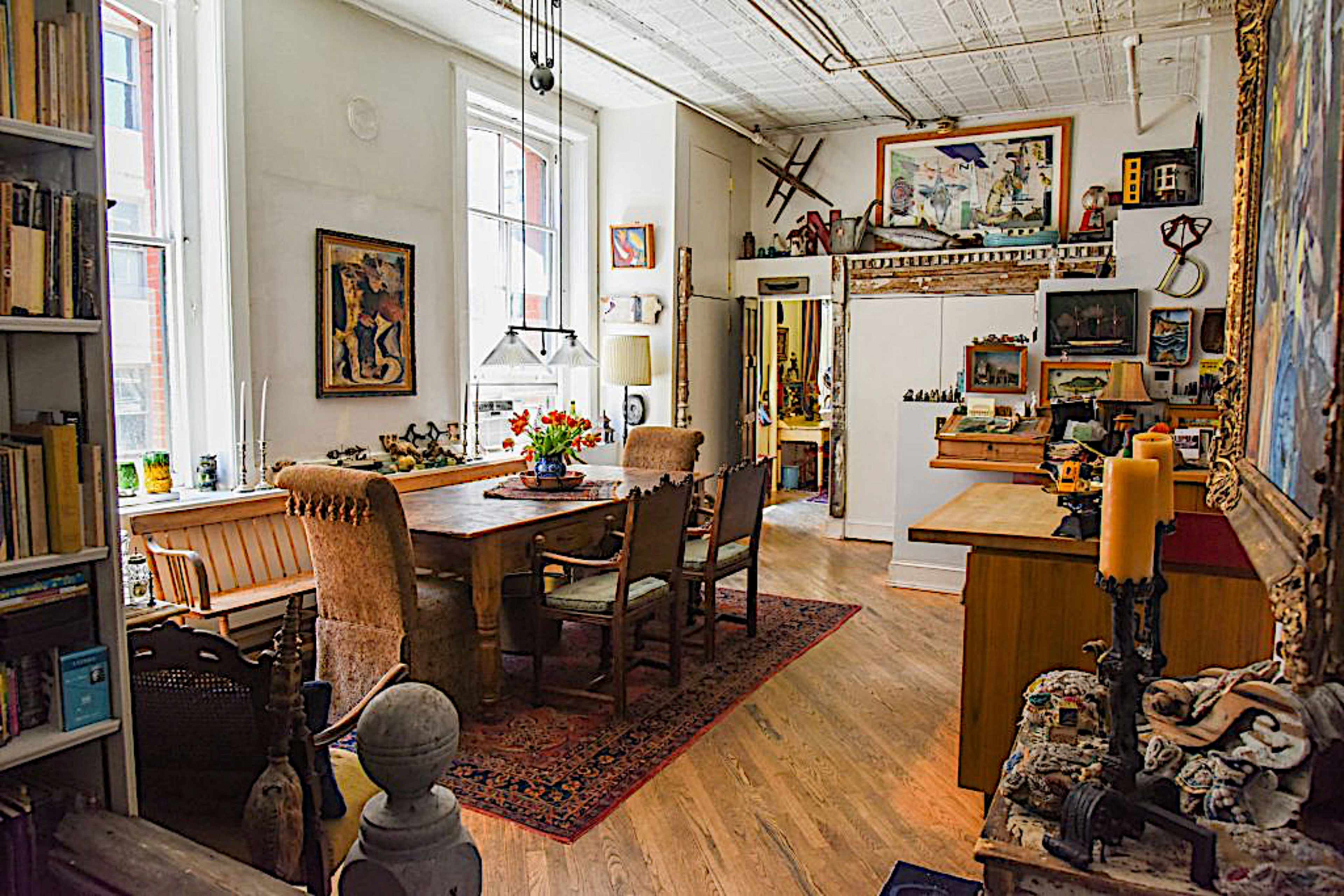 A well-furnished room with a dining table, chairs, artwork on the walls, and various decorative items displayed on surfaces.