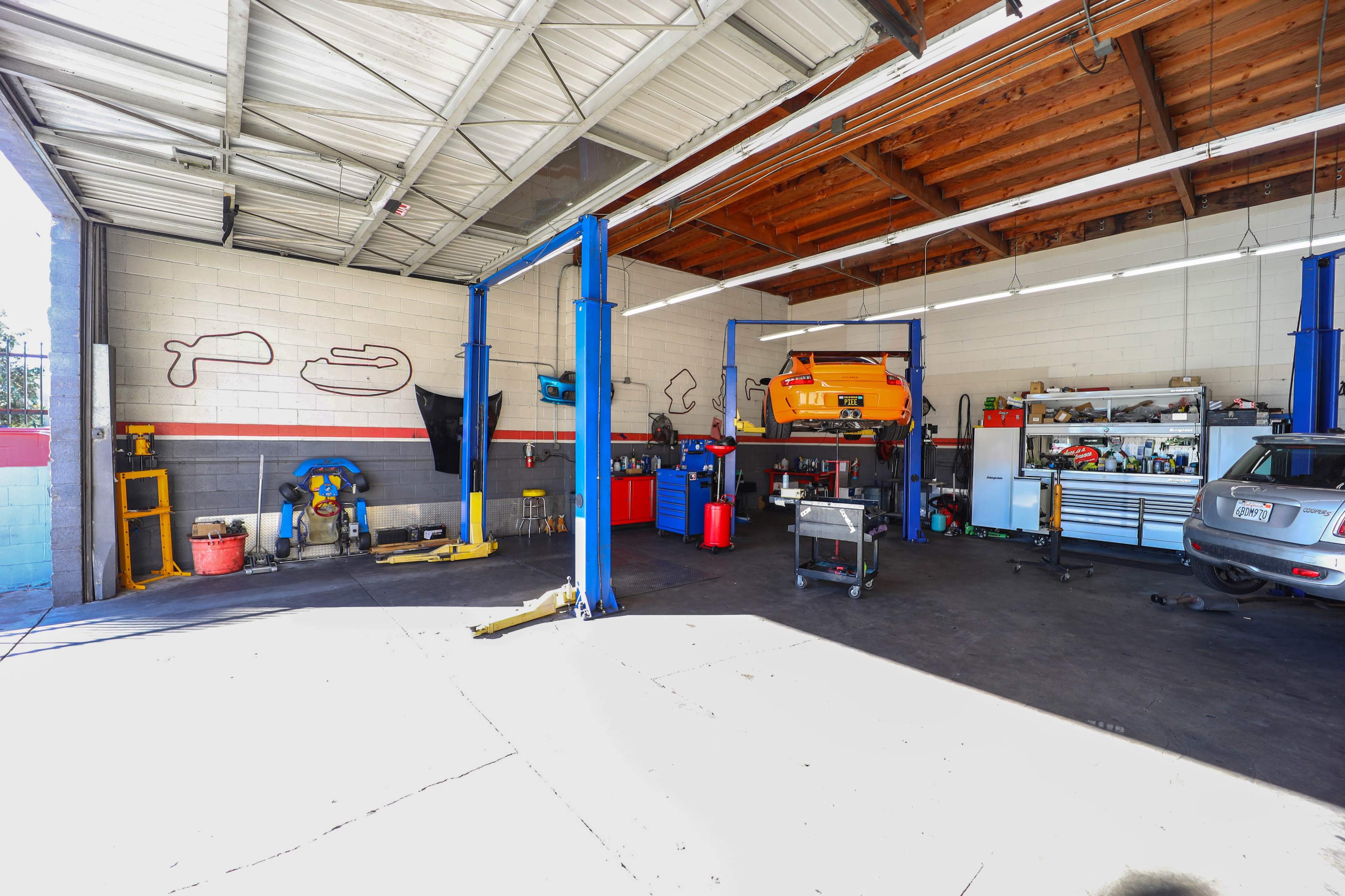 An automotive garage with a vehicle on a lift, various tools and equipment organized on shelves, and a large workspace area.