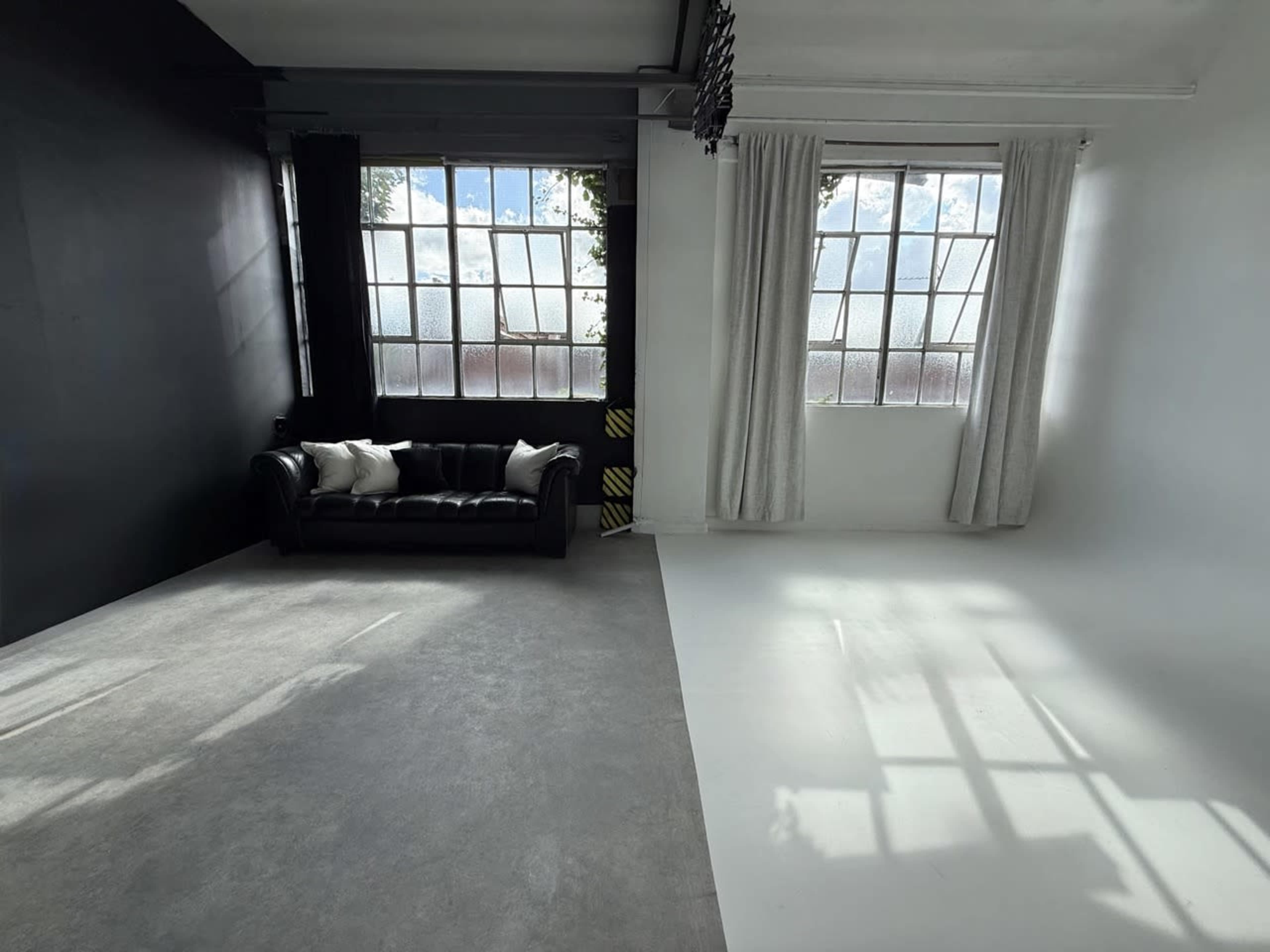 The image shows a modern studio with a black wall on one side, a leather couch with pillows, and large windows allowing natural light to enter.