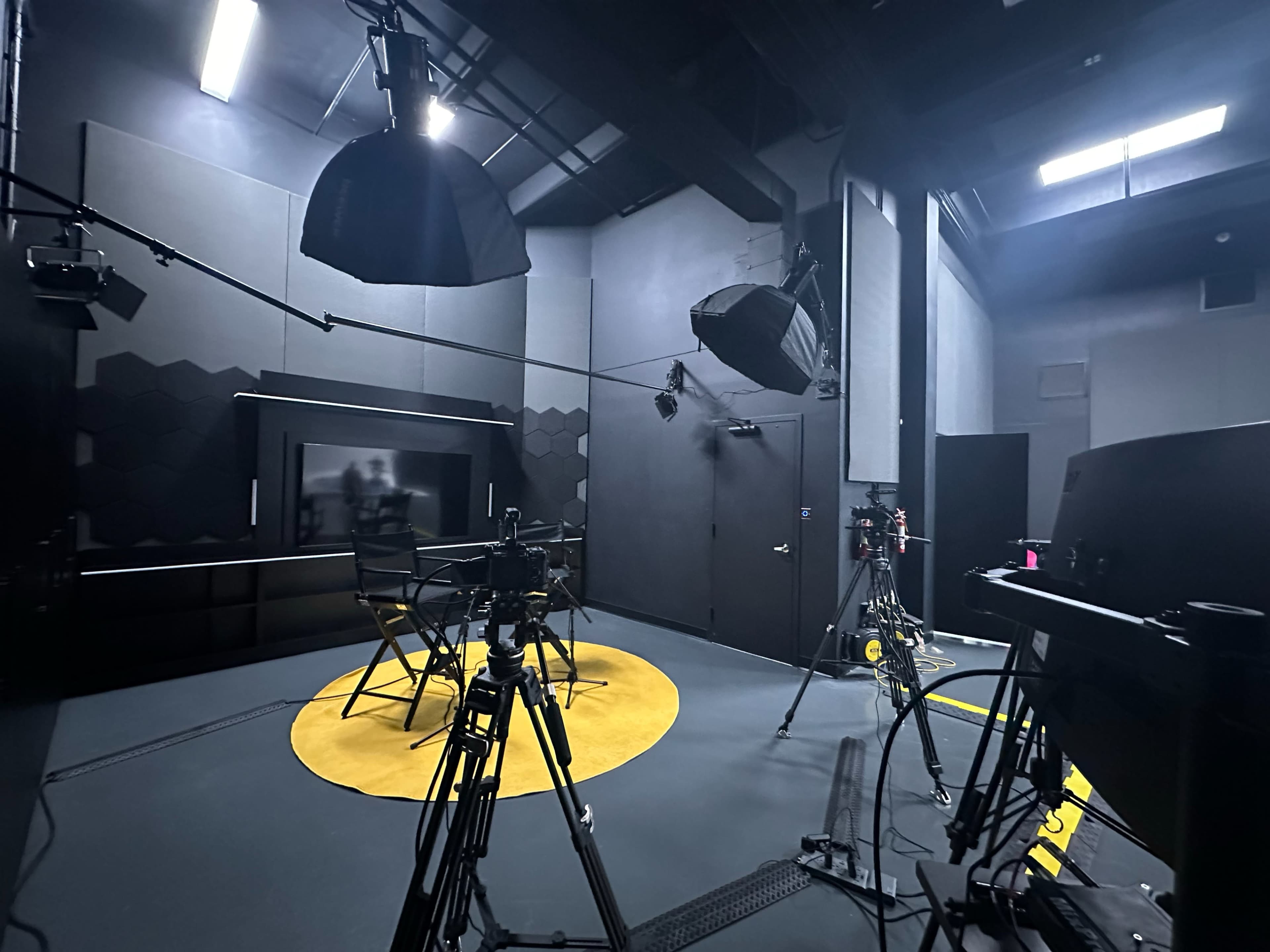 The image shows a dimly lit studio setup with various cameras and lighting equipment arranged around a central circular yellow area on the floor.
