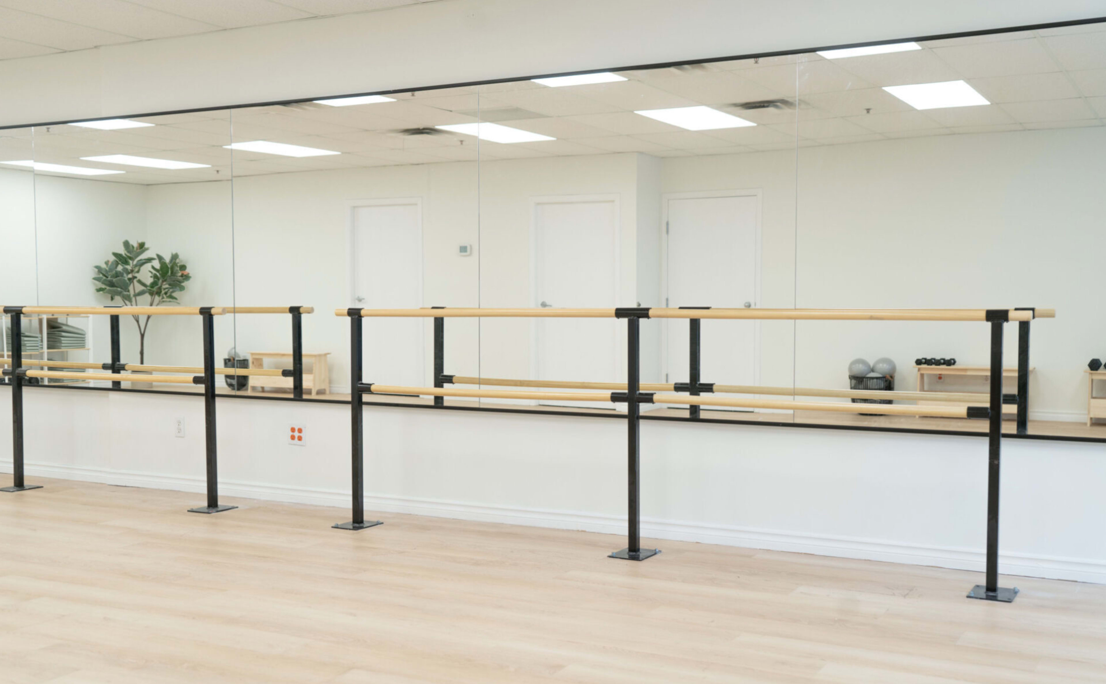 The image shows a spacious ballet studio with a wooden barre, mirrors on the wall, and exercise equipment in the background.