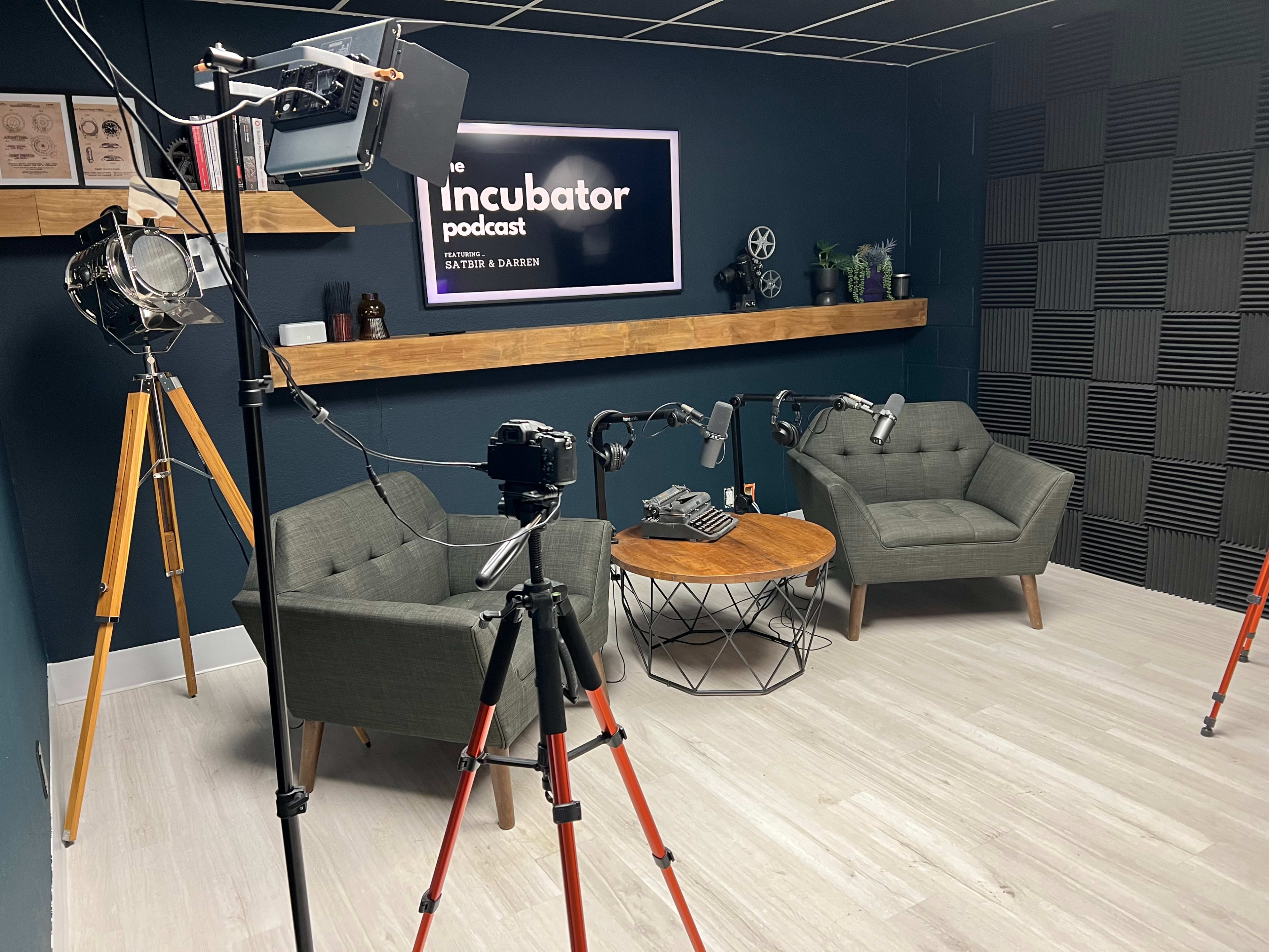 A podcast recording studio featuring two gray armchairs, a round coffee table, and various filming equipment.