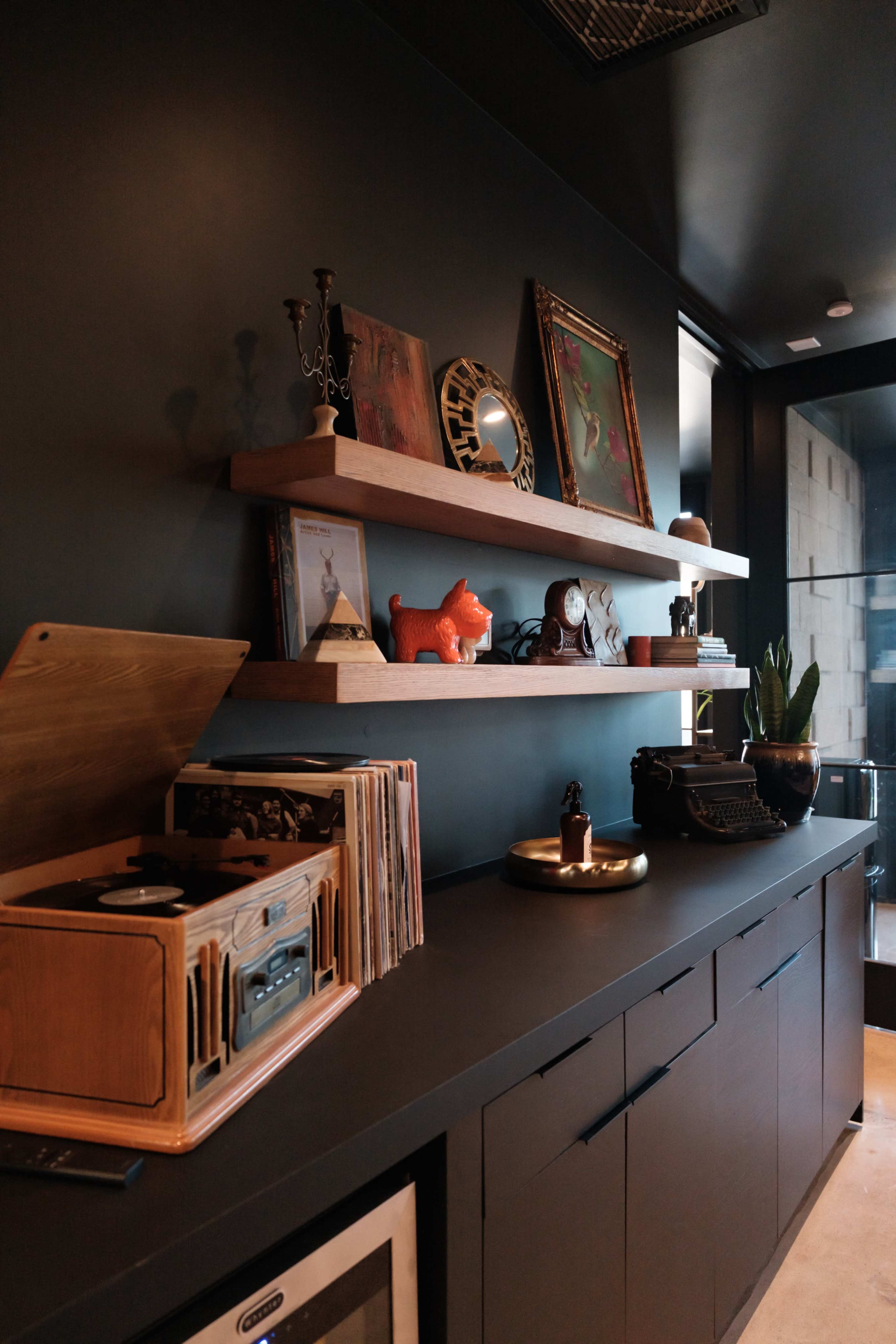 The image shows a modern shelf display with decorative items, a record player, and vinyl records against a dark wall.