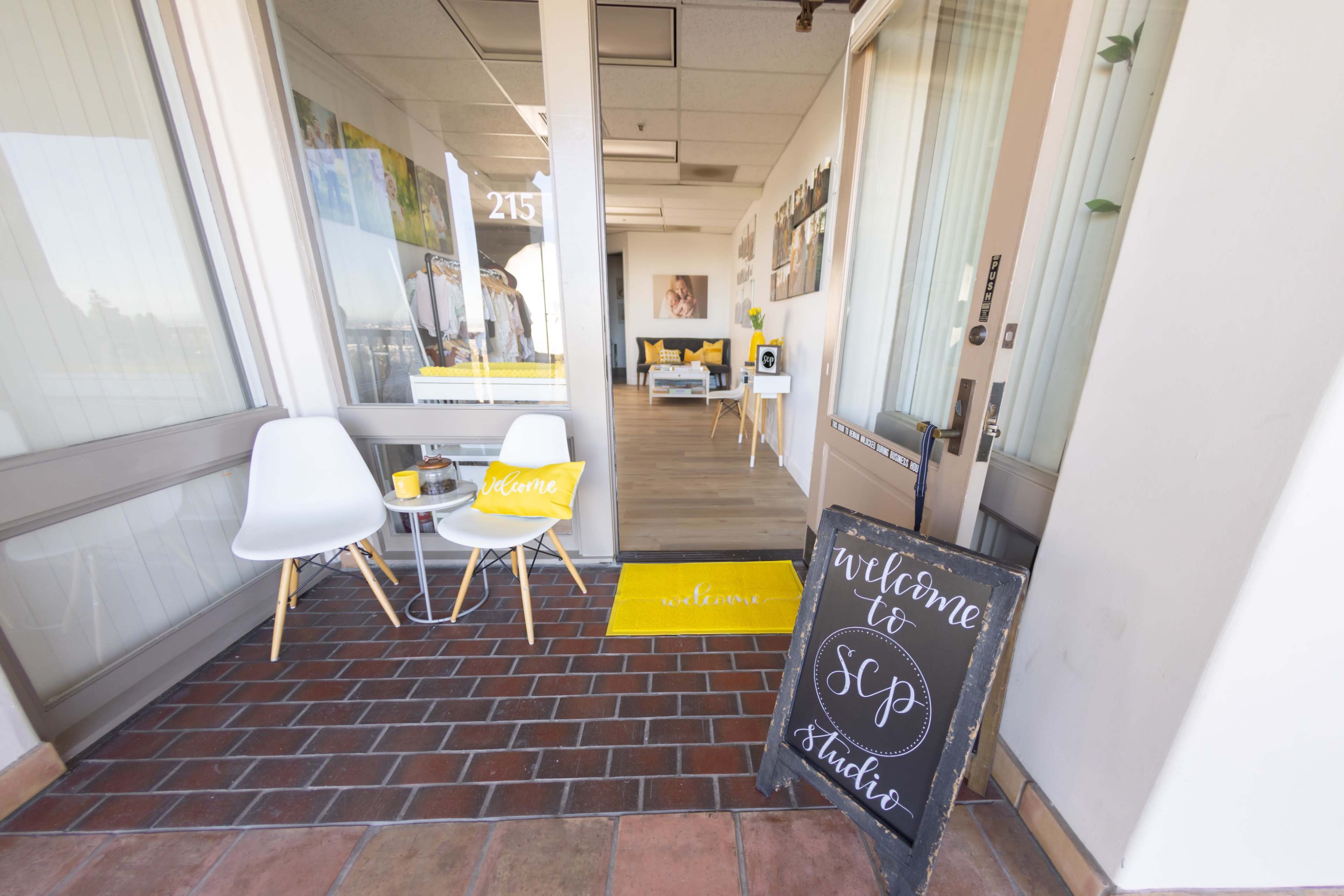 The entrance to a studio features two white chairs, a welcome mat, and a sign displaying "Welcome to SCP Studio."