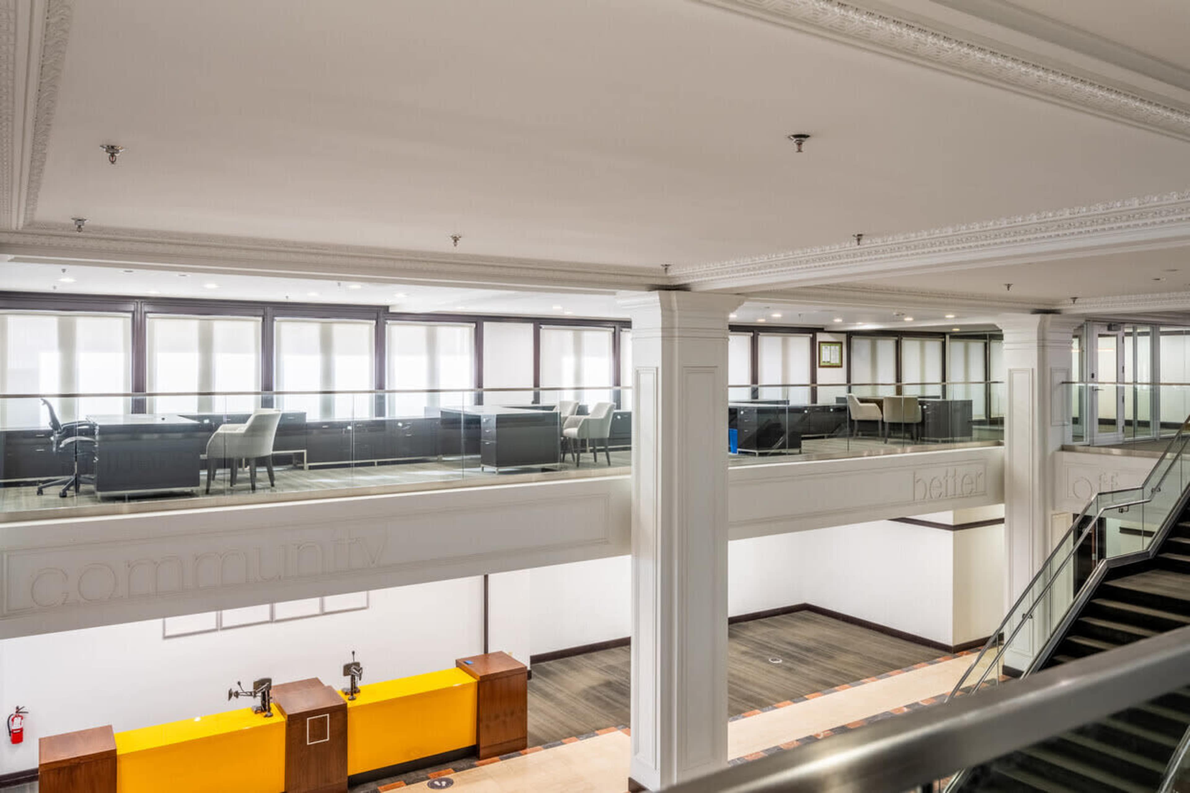 A spacious, multi-level office interior with glass partitions, modern furniture, and a staircase leading to a lower level.