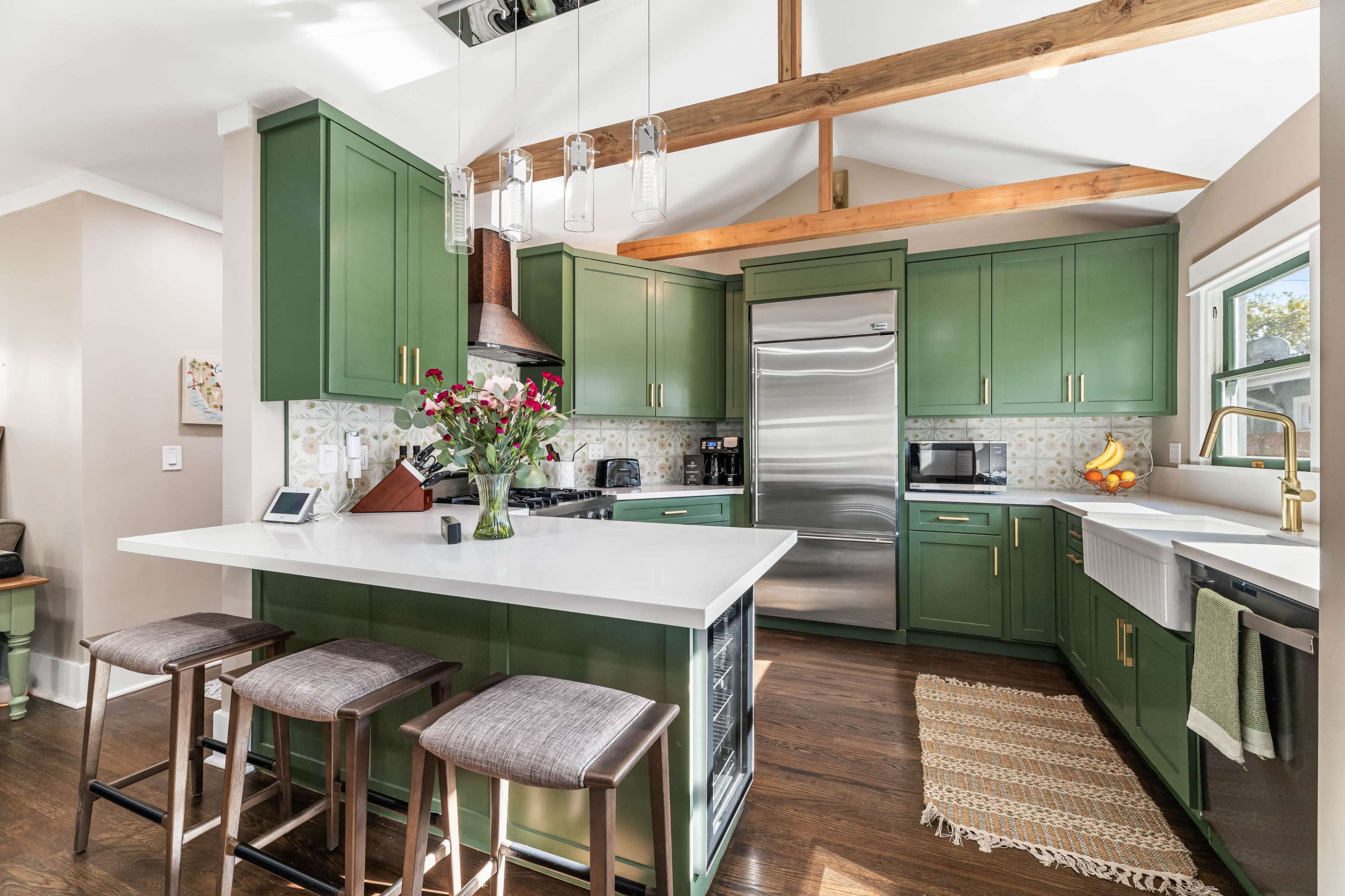 The kitchen features green cabinetry, a white countertop, and a wooden beam ceiling with pendant lighting.