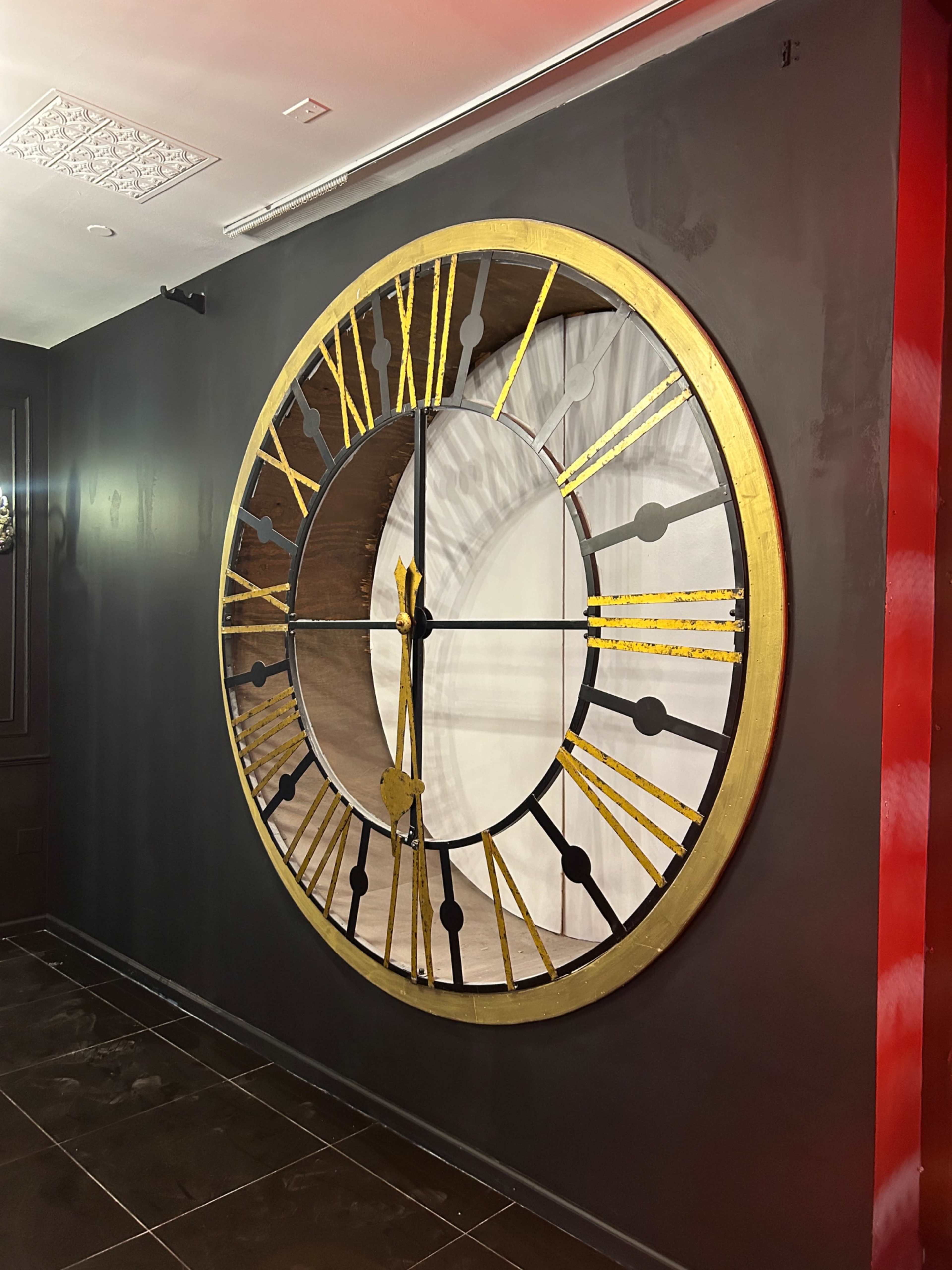 A large, circular wall clock with gold accents and black markings is mounted on a dark wall.
