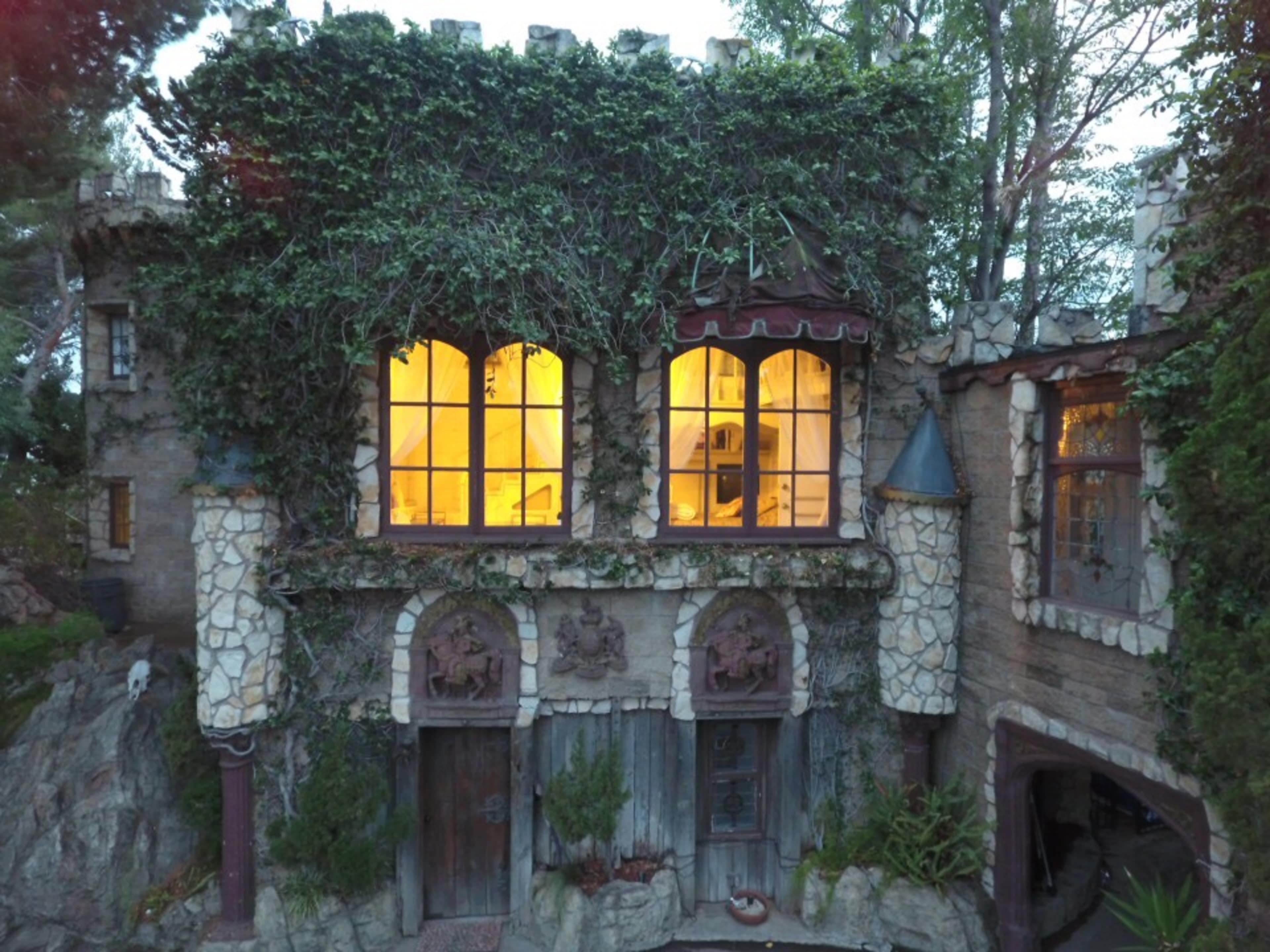 A stone castle-like structure covered in ivy, featuring large windows that emit a warm glow.