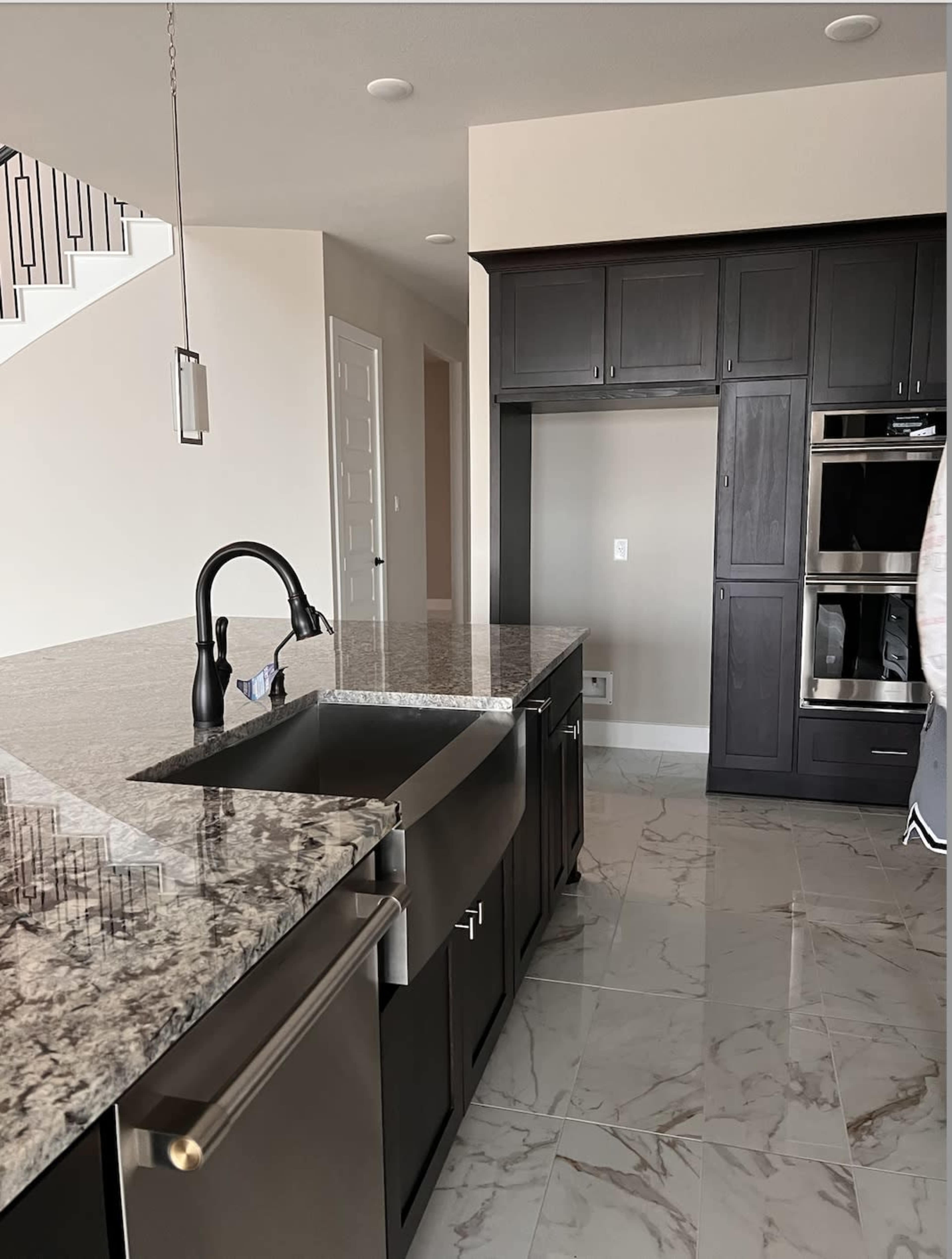 The image shows a modern kitchen featuring a large granite countertop island with a sink, dark cabinetry, and stainless steel appliances.