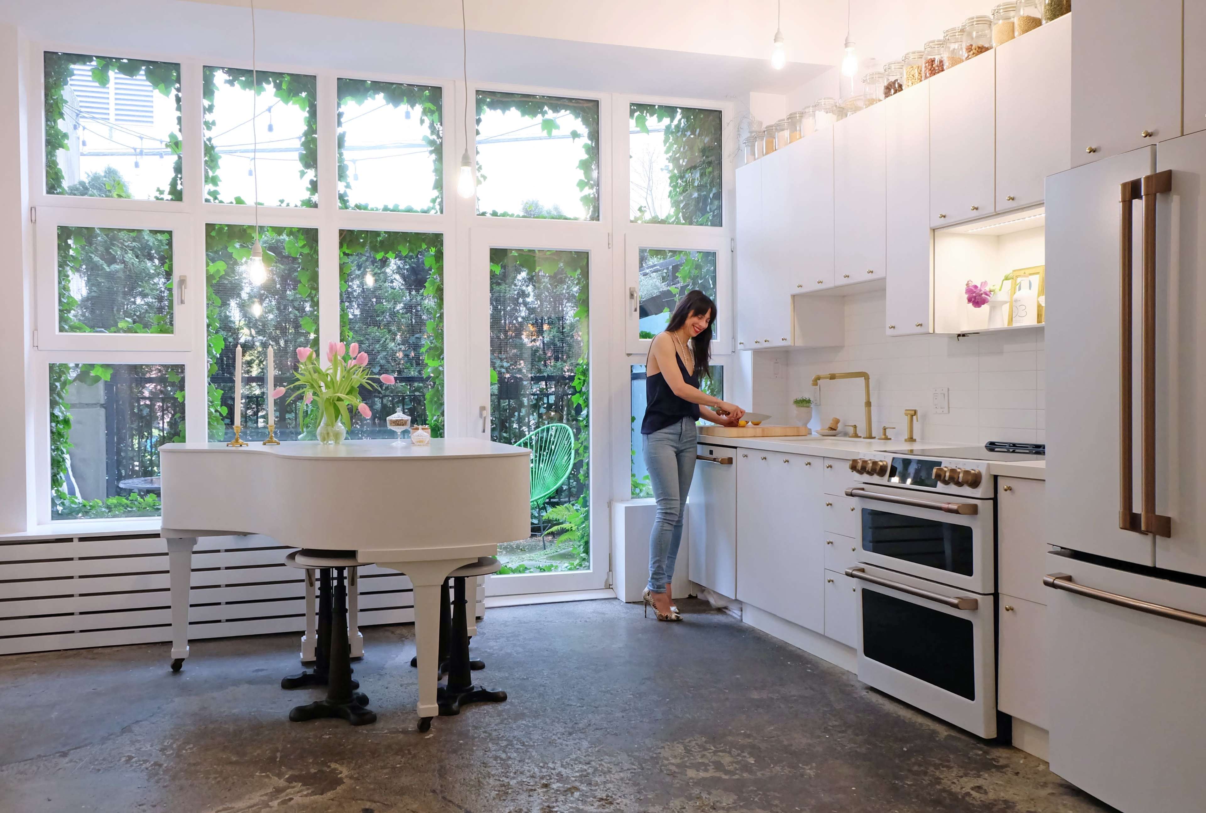 A woman prepares food in a modern kitchen with large windows overlooking a garden.