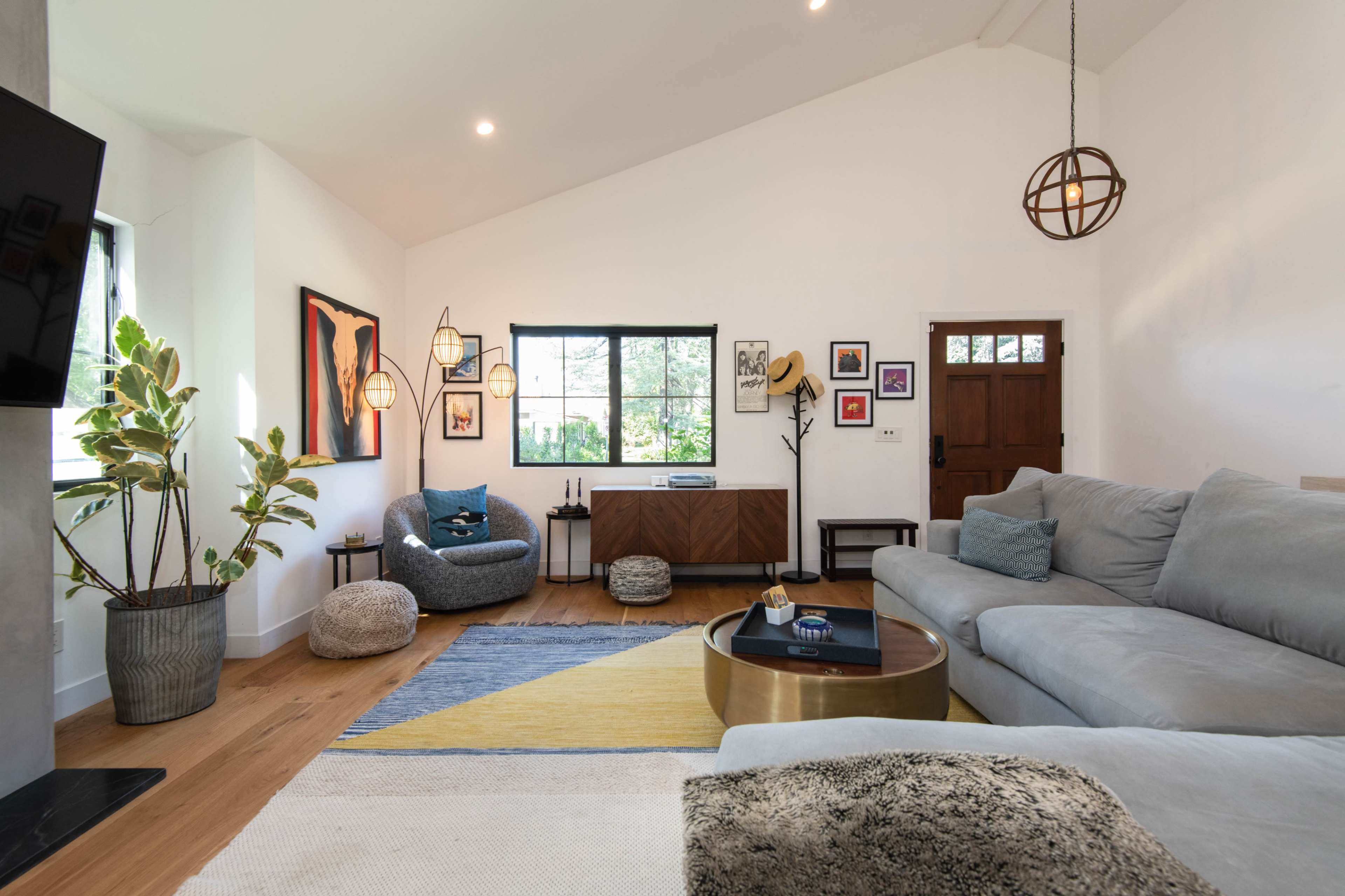 A modern living room featuring a gray sectional sofa, a circular coffee table, a large window, and various decorative art pieces on the walls.