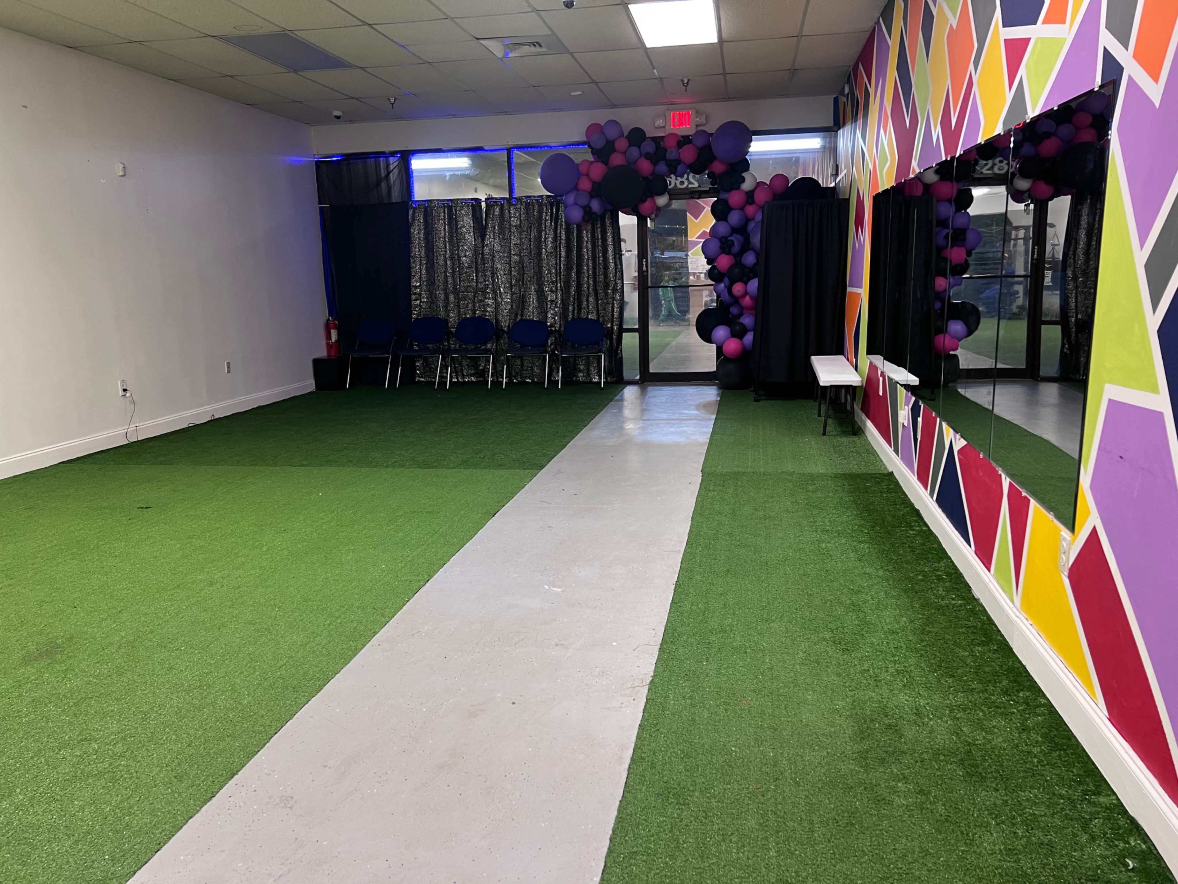 A large room with green turf flooring, a concrete pathway running through the center, and colorful walls decorated with geometric patterns.