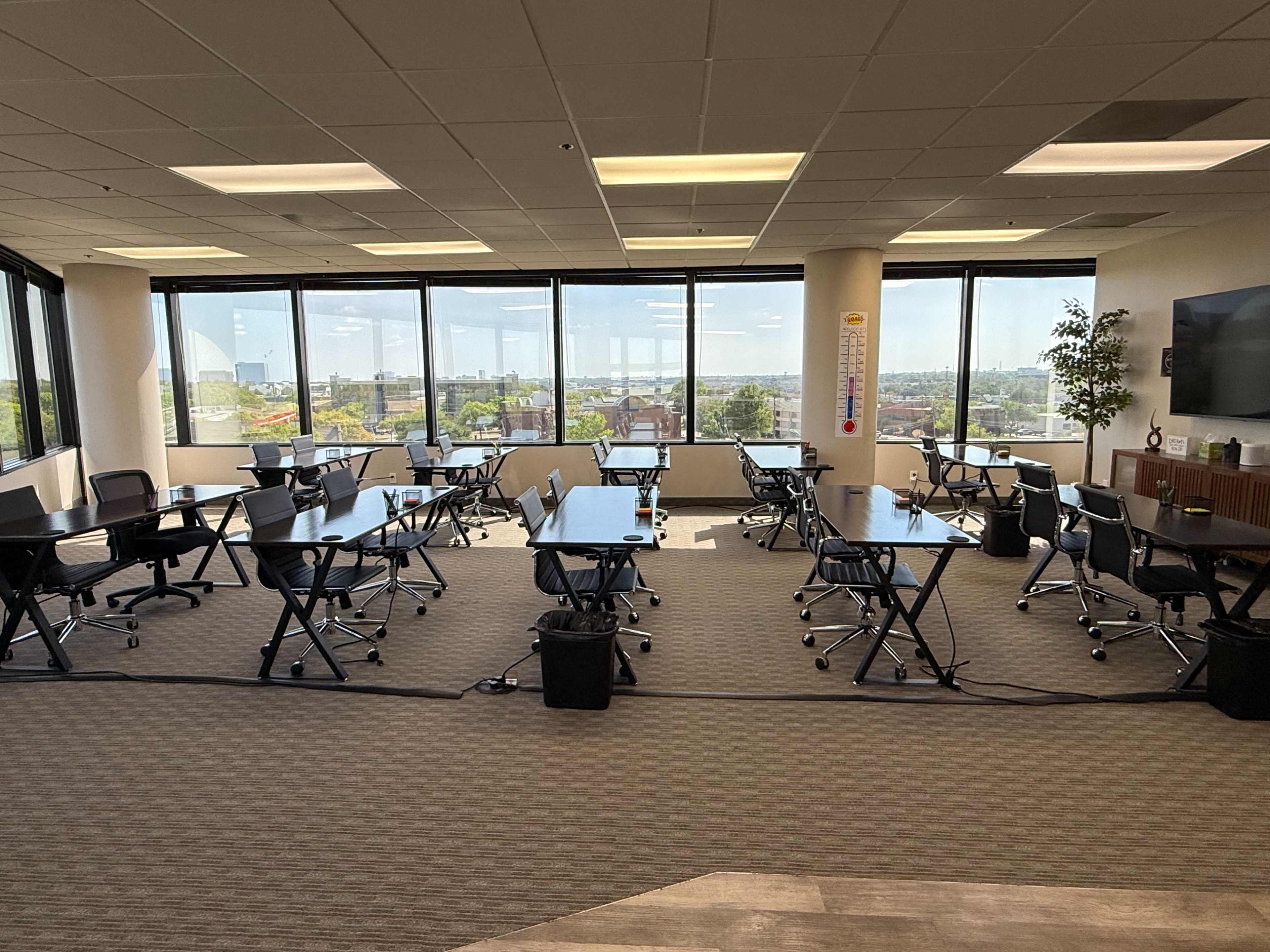 The image shows an office space with multiple foldable tables and chairs arranged in a room with large windows overlooking a cityscape.