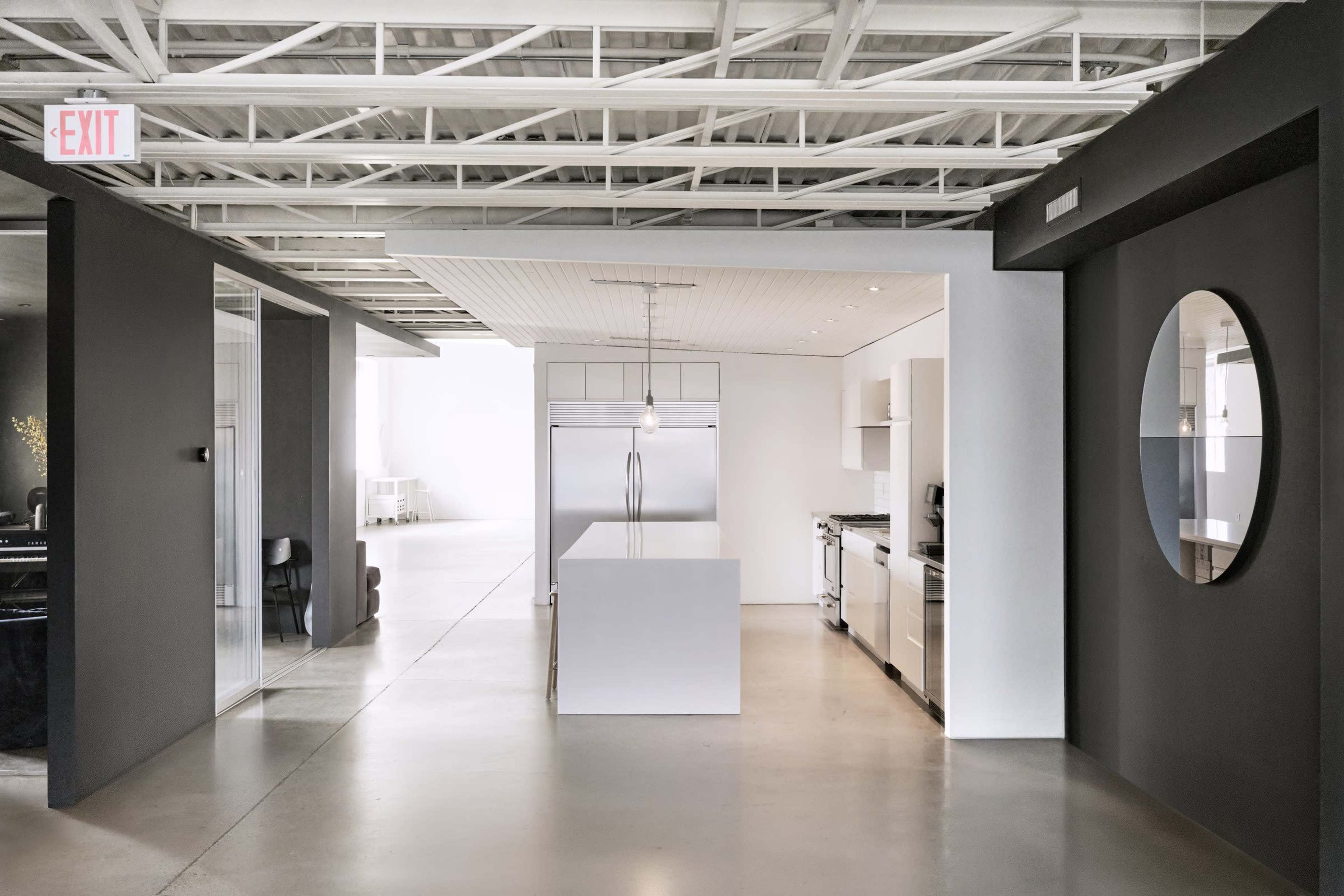 The image shows a modern kitchen with a centralized island, stainless steel appliances, and an open layout connecting to a spacious dining area.