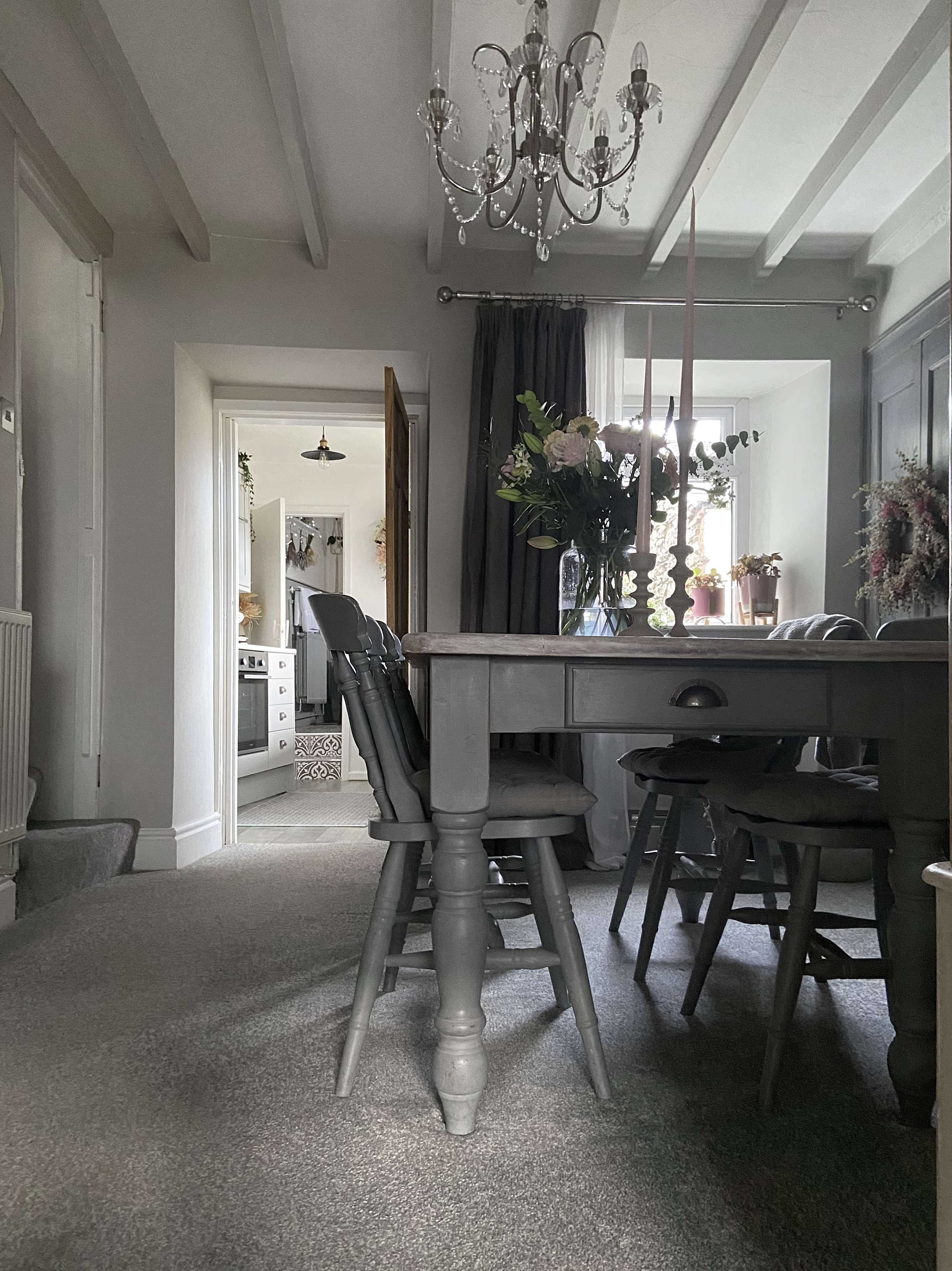 A gray dining table and chairs are set in a well-lit room featuring a chandelier and a view into an adjoining space.