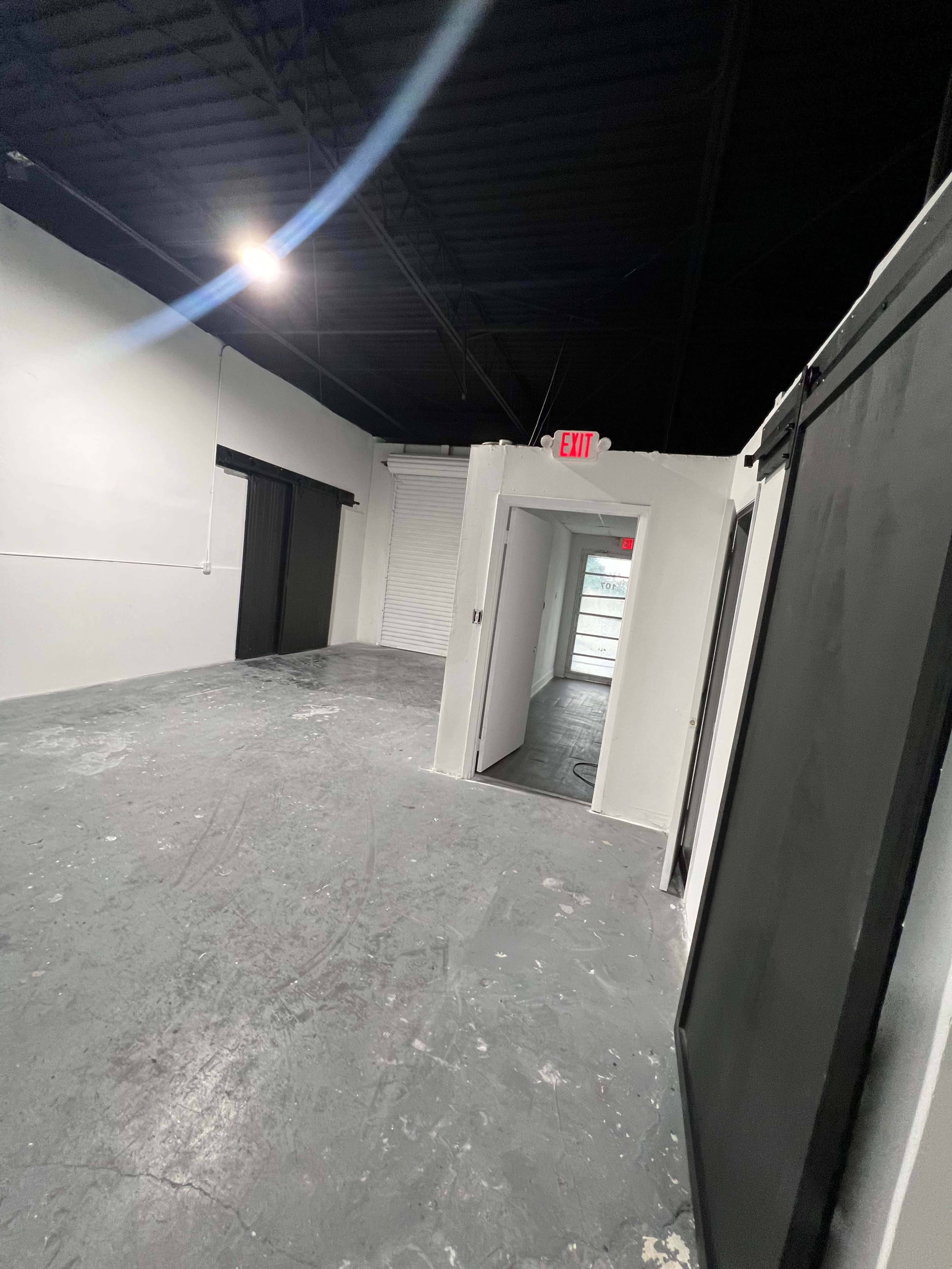 The image shows an empty interior space with white walls, a concrete floor, and several doorways leading to other areas.
