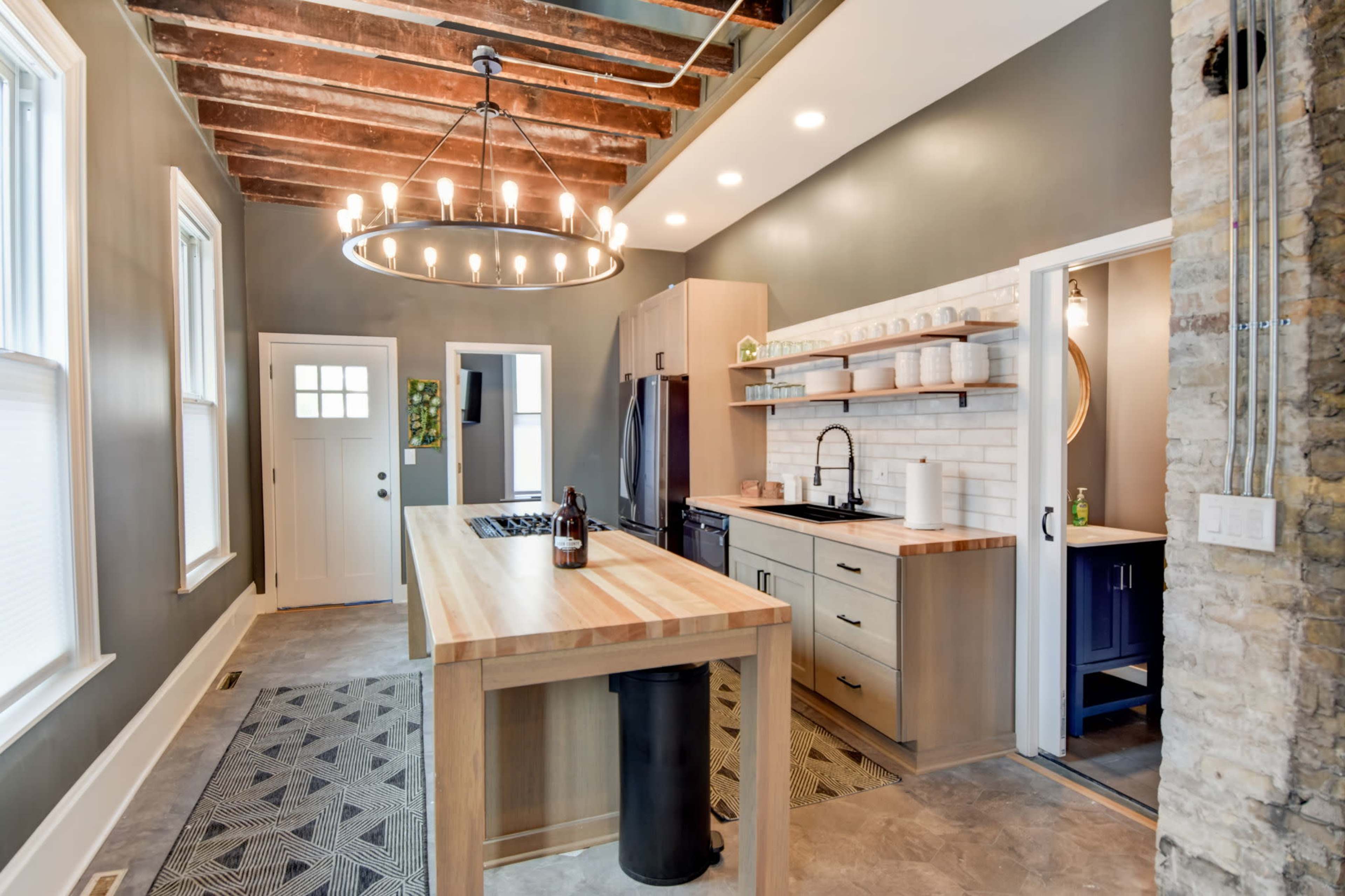 A modern kitchen featuring a large wooden island, stainless steel appliances, and exposed wooden beams on the ceiling.