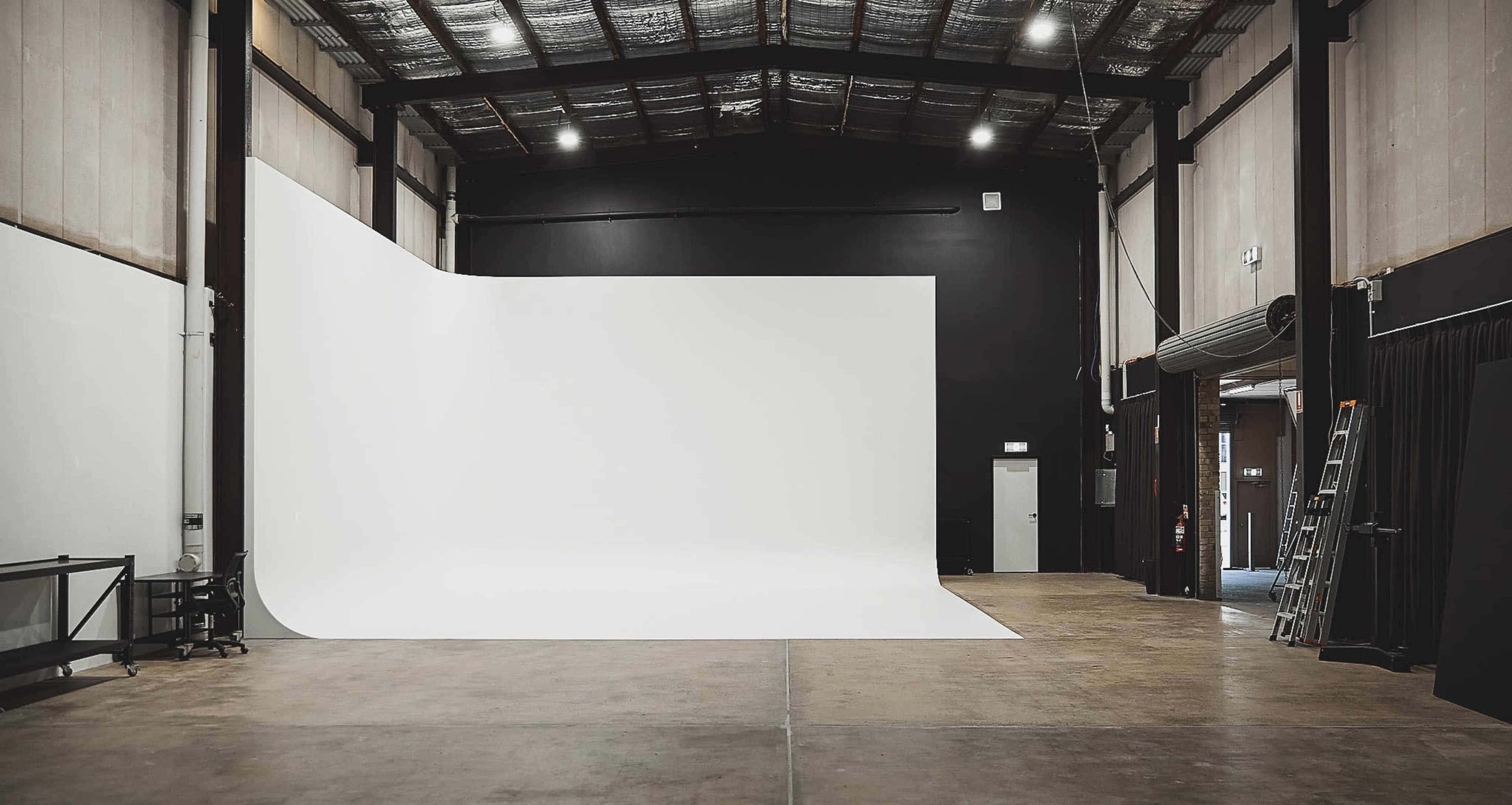 A spacious photography studio featuring a large white backdrop and a polished concrete floor.