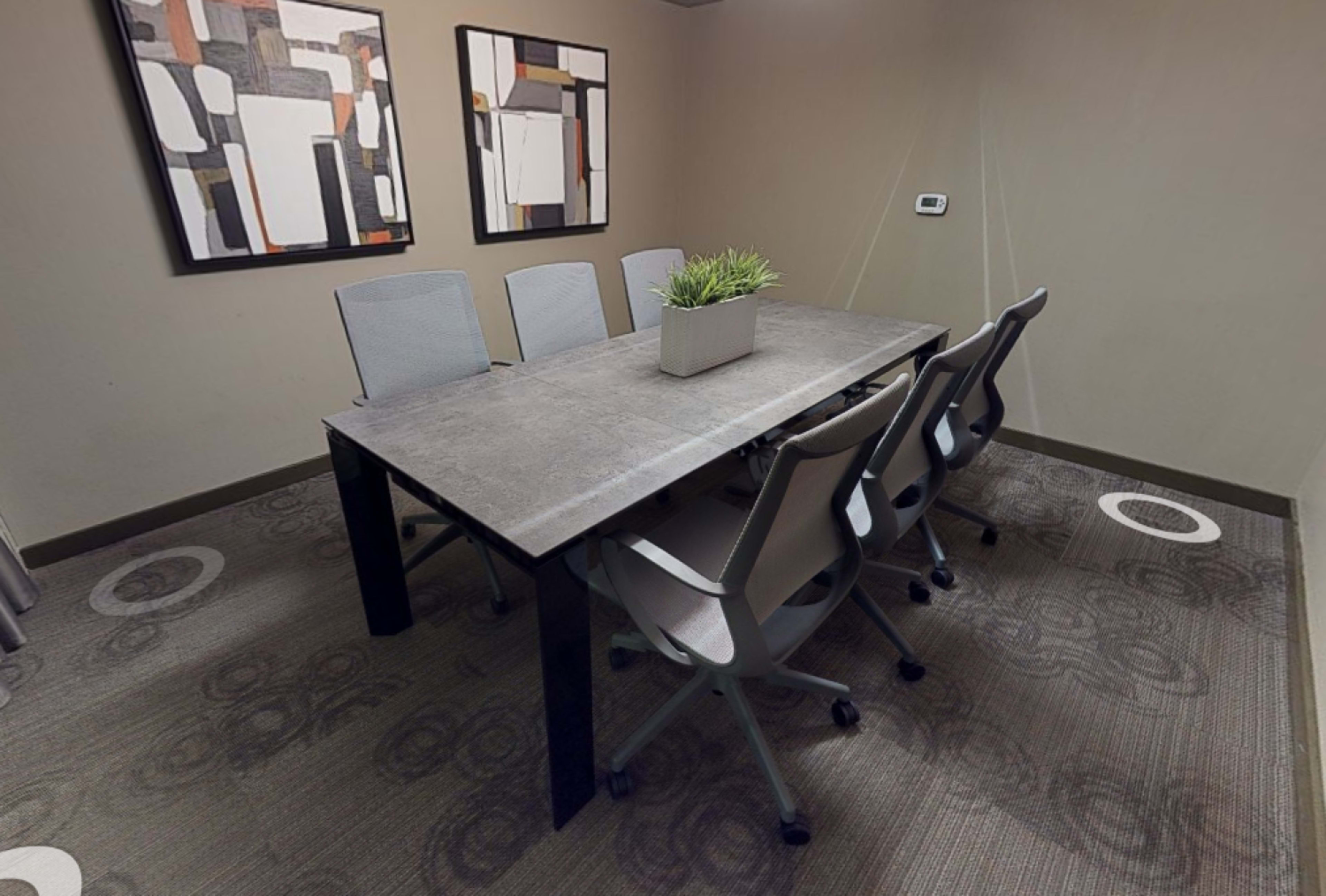 The image shows a conference room with a large table surrounded by six ergonomic chairs and two abstract artworks on the walls.