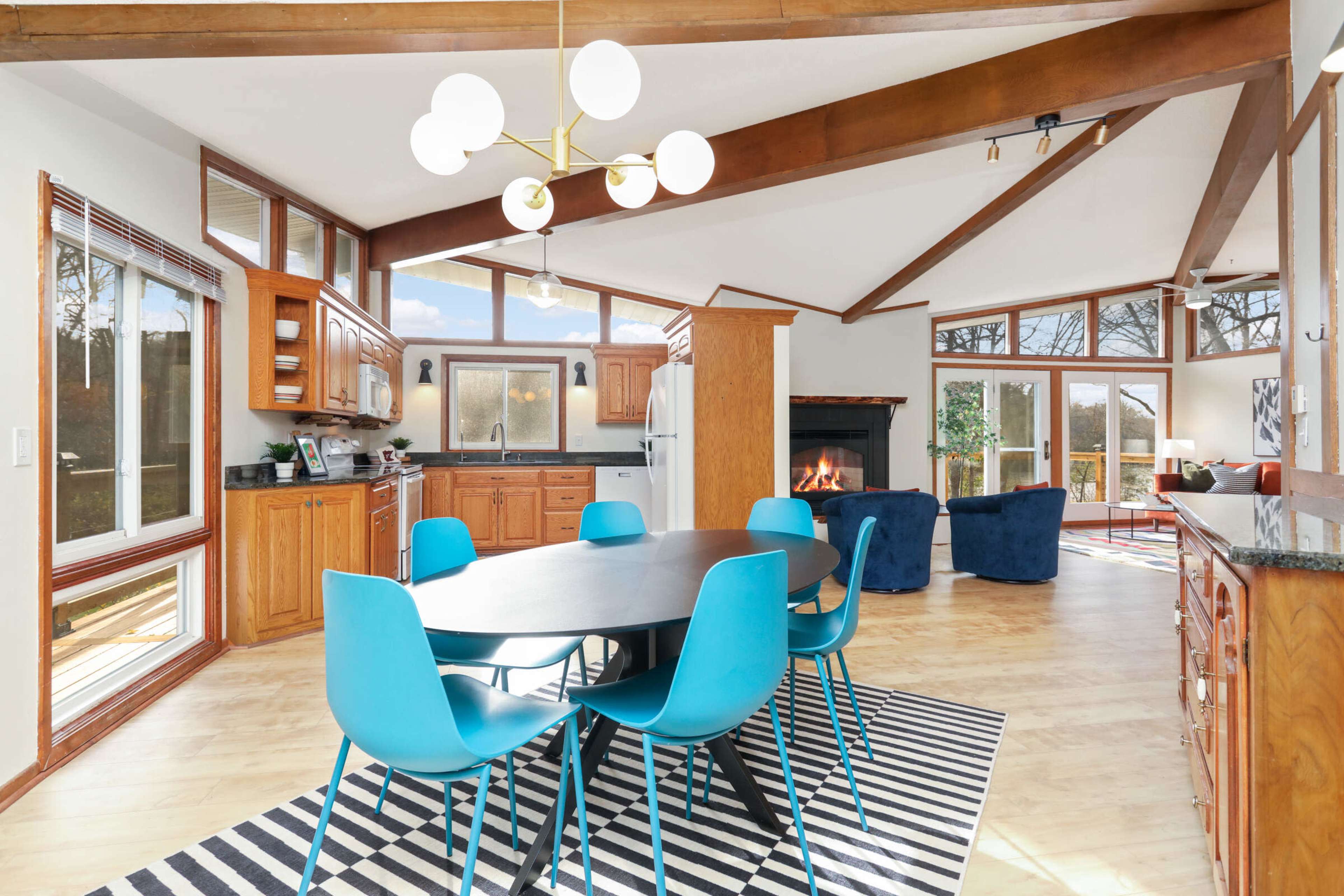 A spacious, open-concept living area features a dining table with blue chairs, a kitchen with wooden cabinets, and a cozy seating area with a fireplace.