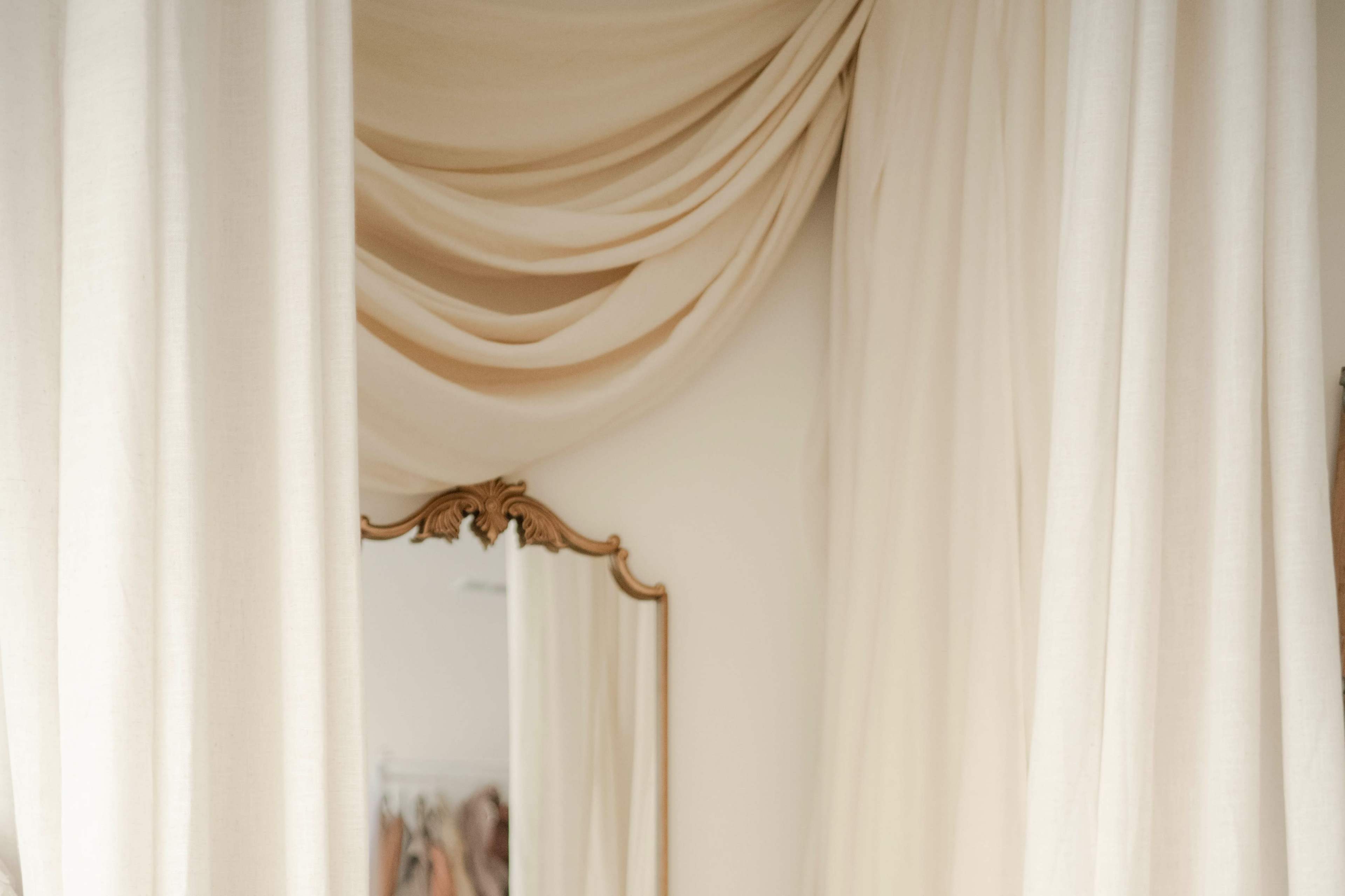 The image displays a decorative mirror surrounded by draped beige fabric.