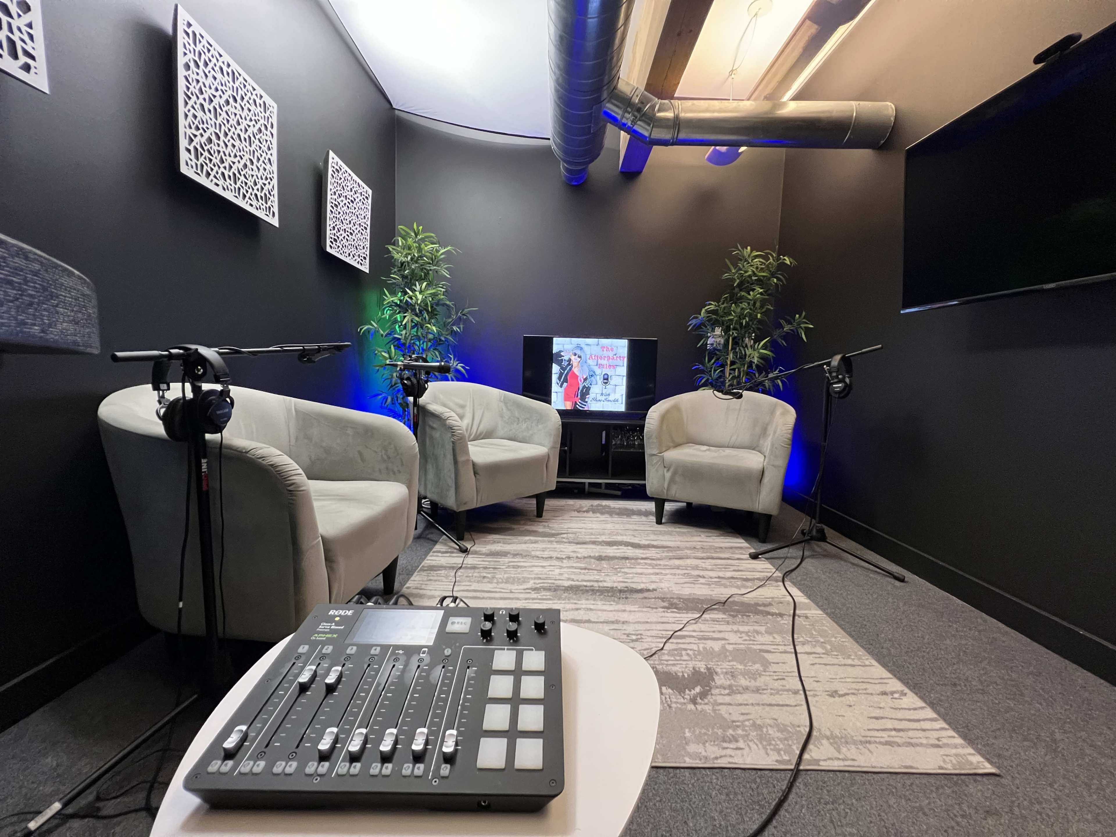 The image shows a small recording studio with two armchairs, a television, and audio equipment on a table.