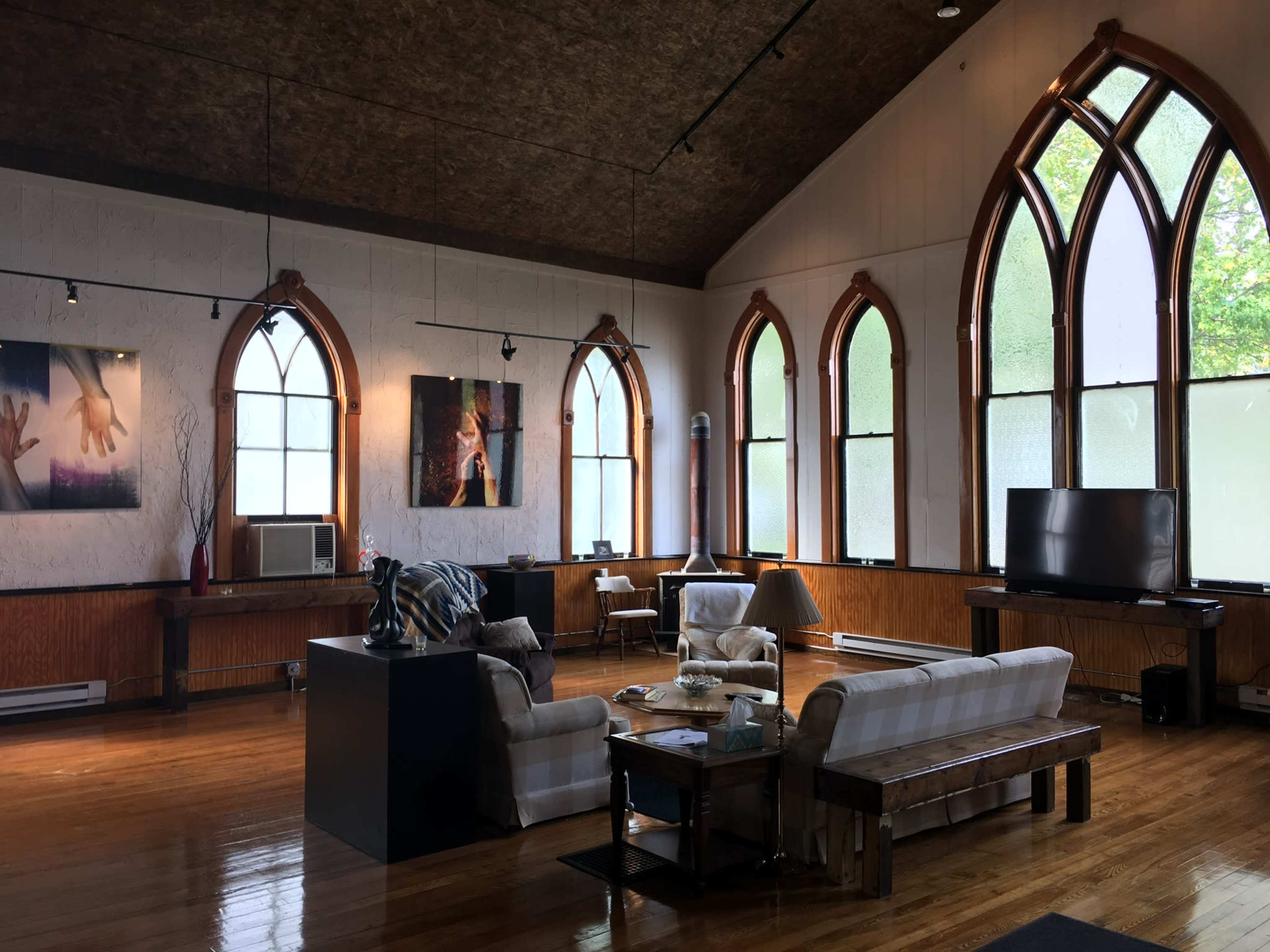 A spacious room with high ceilings, large arched windows, wooden flooring, and a seating area featuring a couch and coffee table.