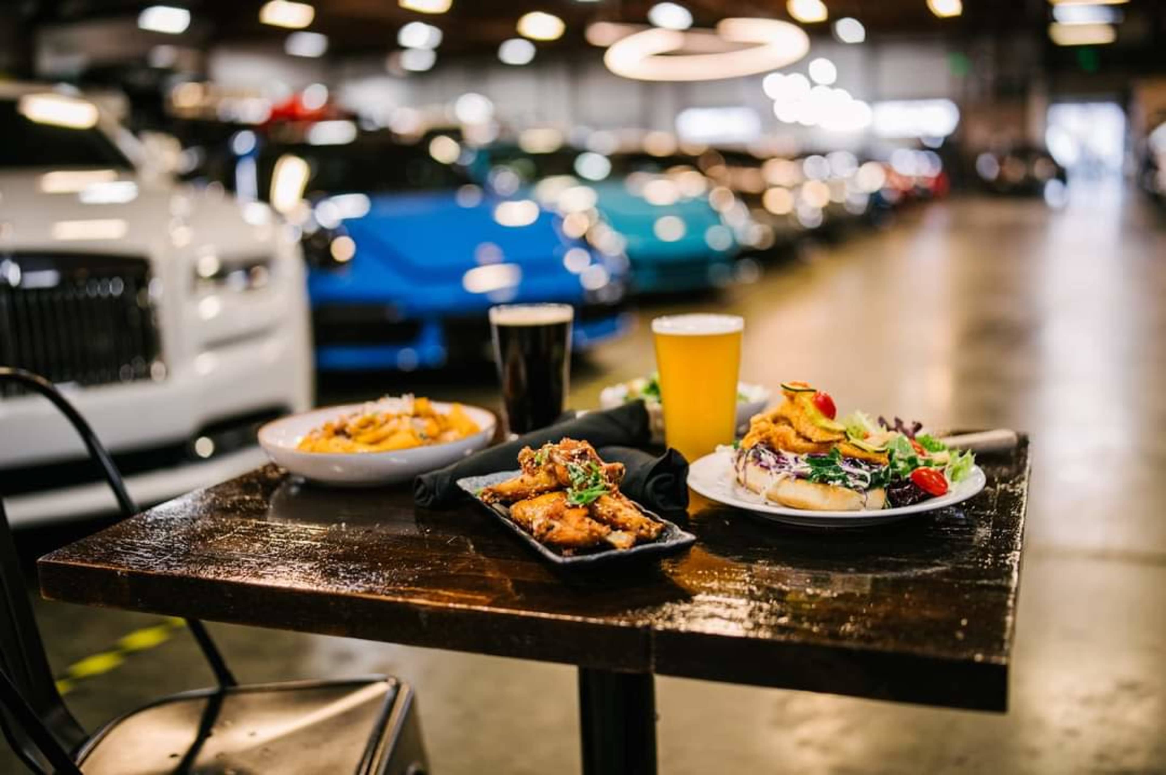 A wooden table in a car showroom displays a selection of dishes alongside two glasses of beer.