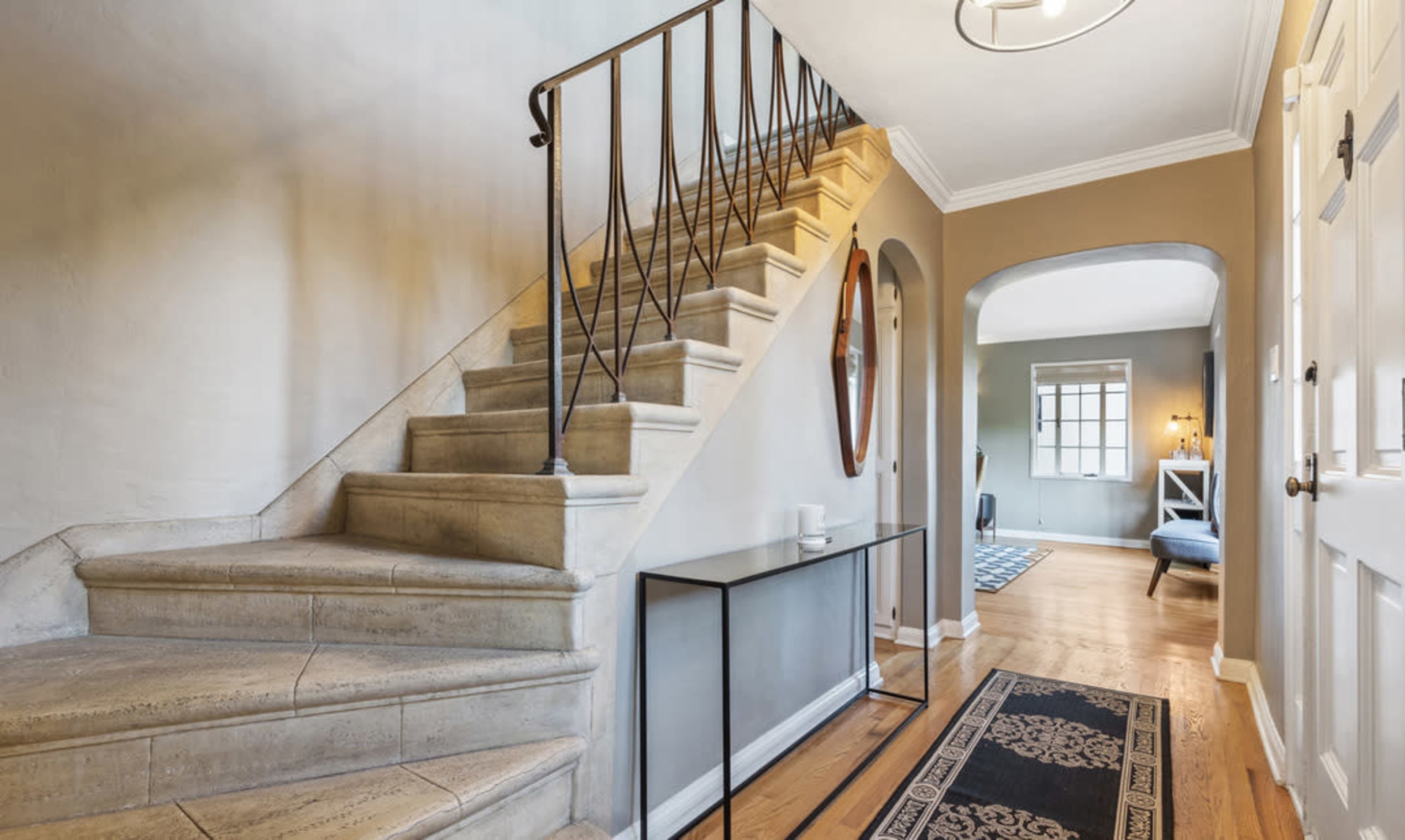 A hallway with a staircase on the left, a decorative mirror on the wall, and a console table beside the entrance door.