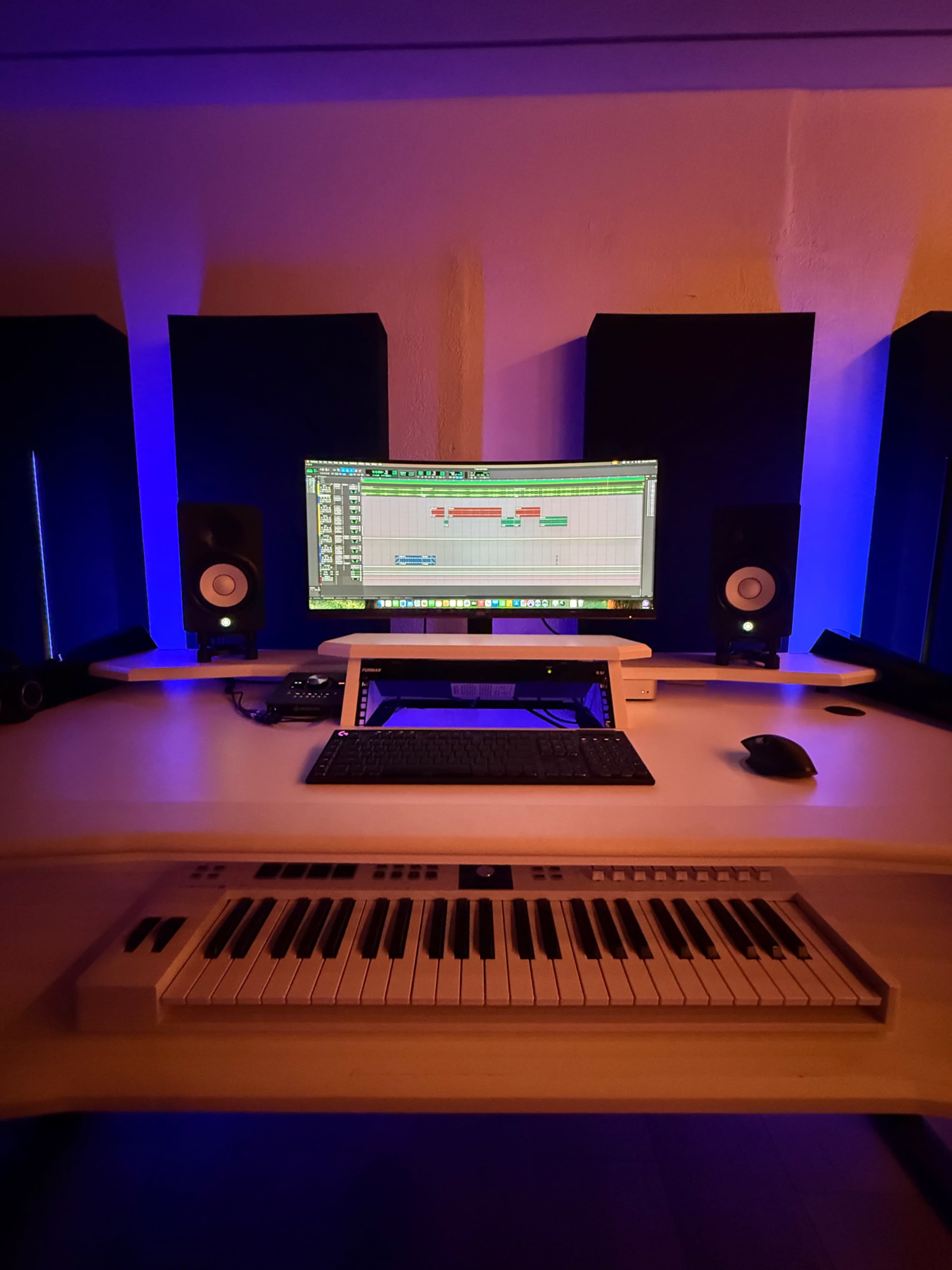 A music production studio is shown, featuring a computer monitor displaying audio tracks, a keyboard, and sound speakers with ambient lighting.