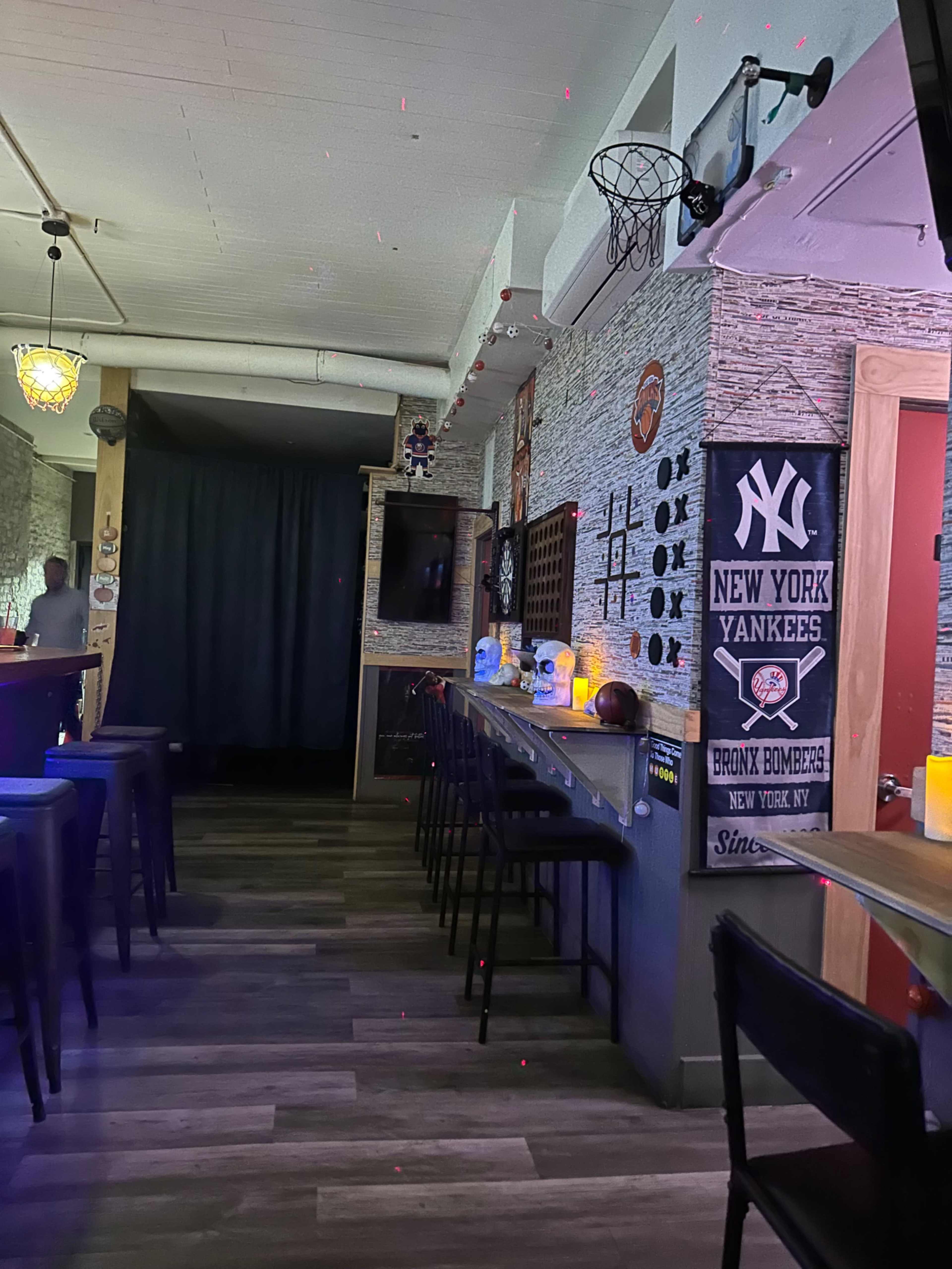 The image shows the interior of a bar with a basketball hoop on the wall, decorated with sports memorabilia and illuminated by soft lighting.