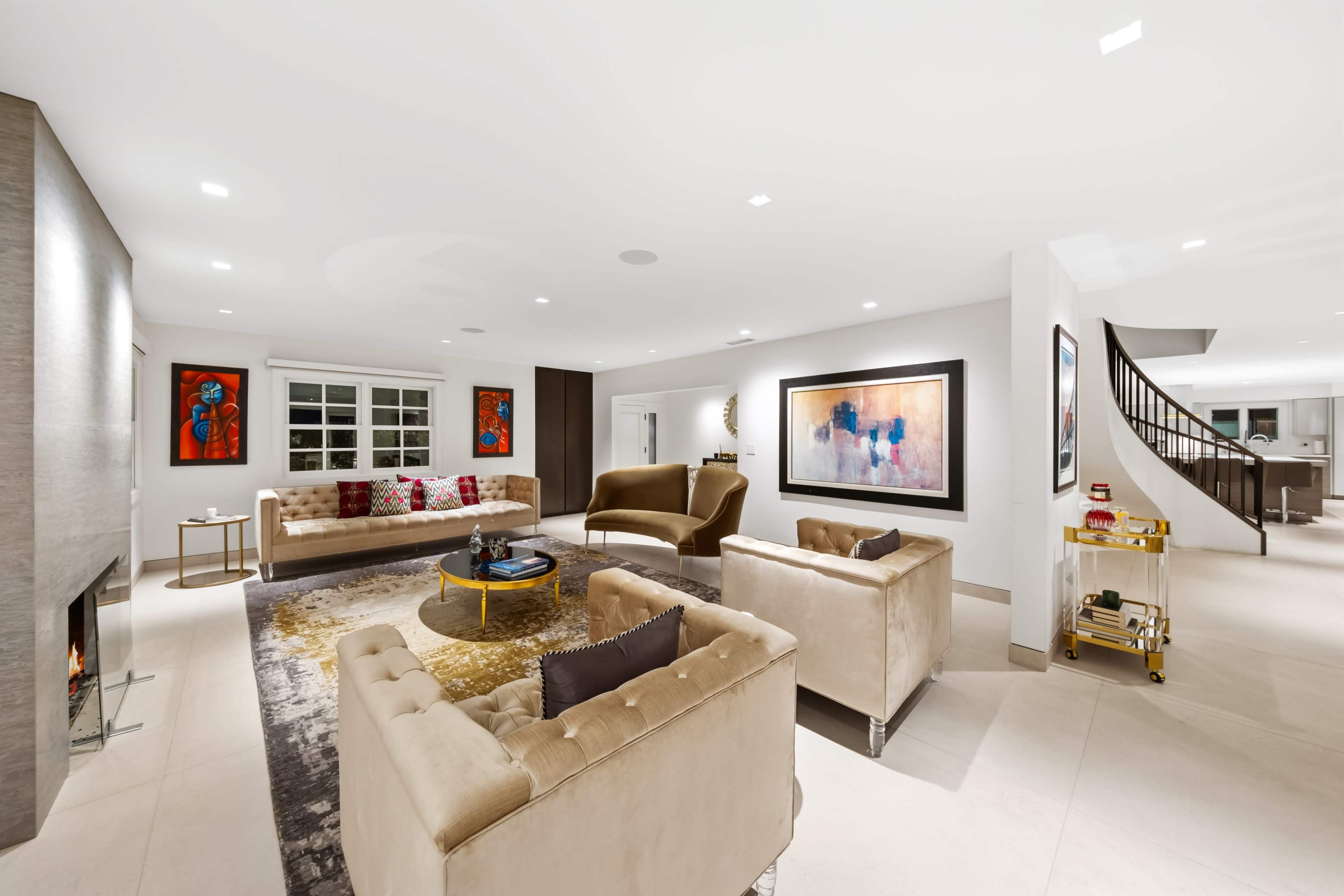 The image shows a modern living room with plush sofas, a round rug, and artwork on the walls, illuminated by recessed lighting.