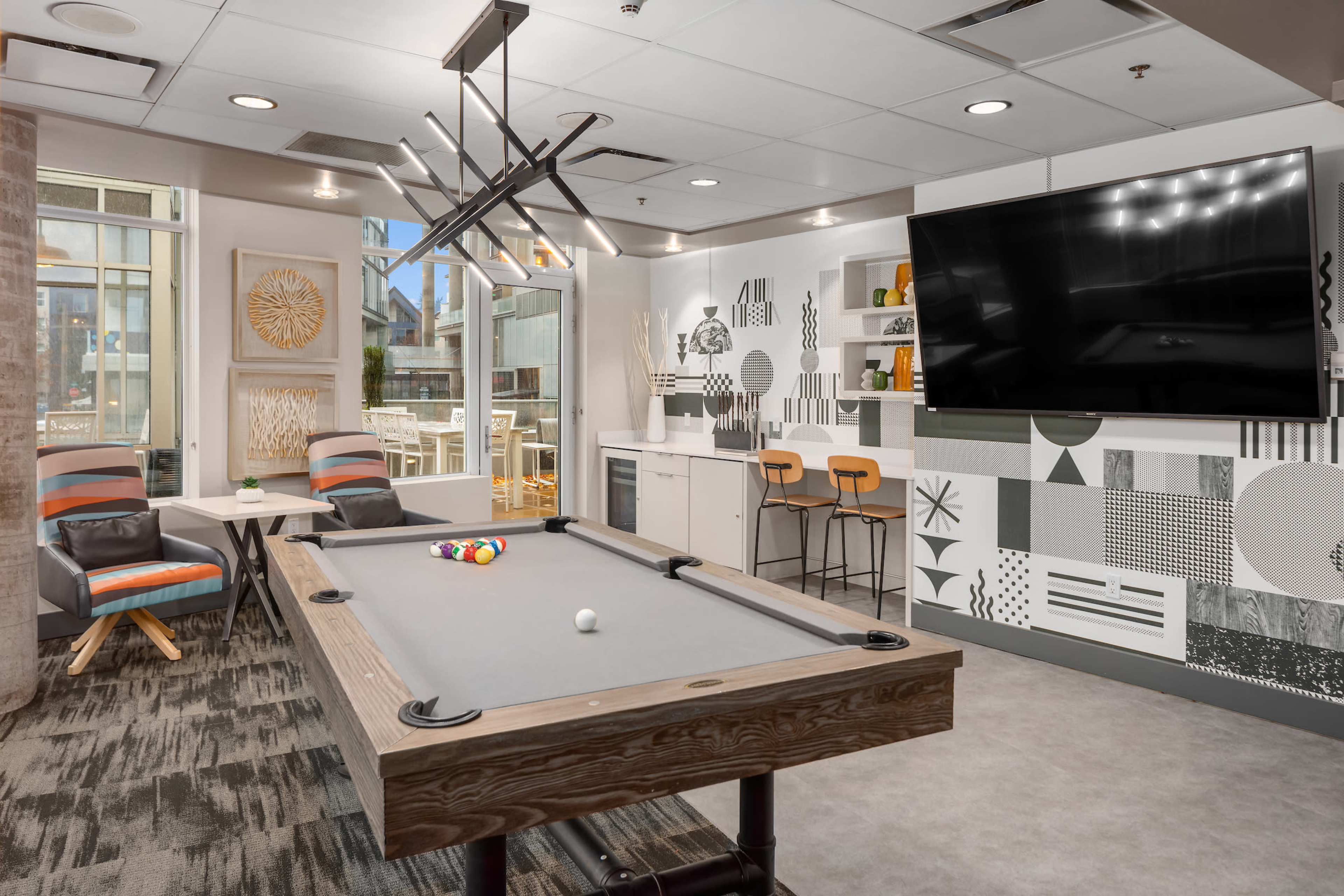A modern game room featuring a pool table, seating area, and a large wall-mounted television with a patterned mural.
