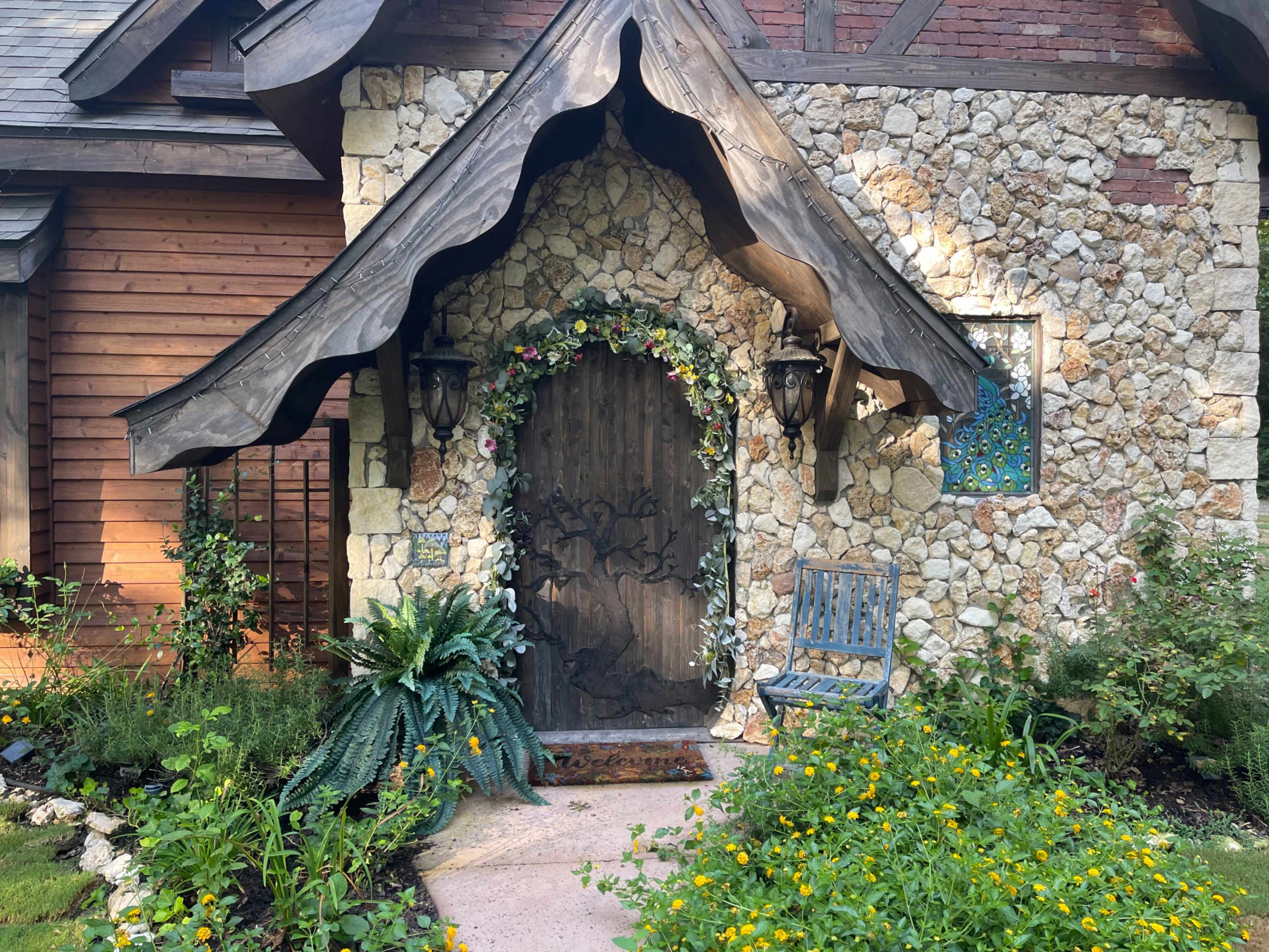 The entrance features a wooden door framed by stone walls, with a decorative archway adorned with flowers and flanked by two lanterns.