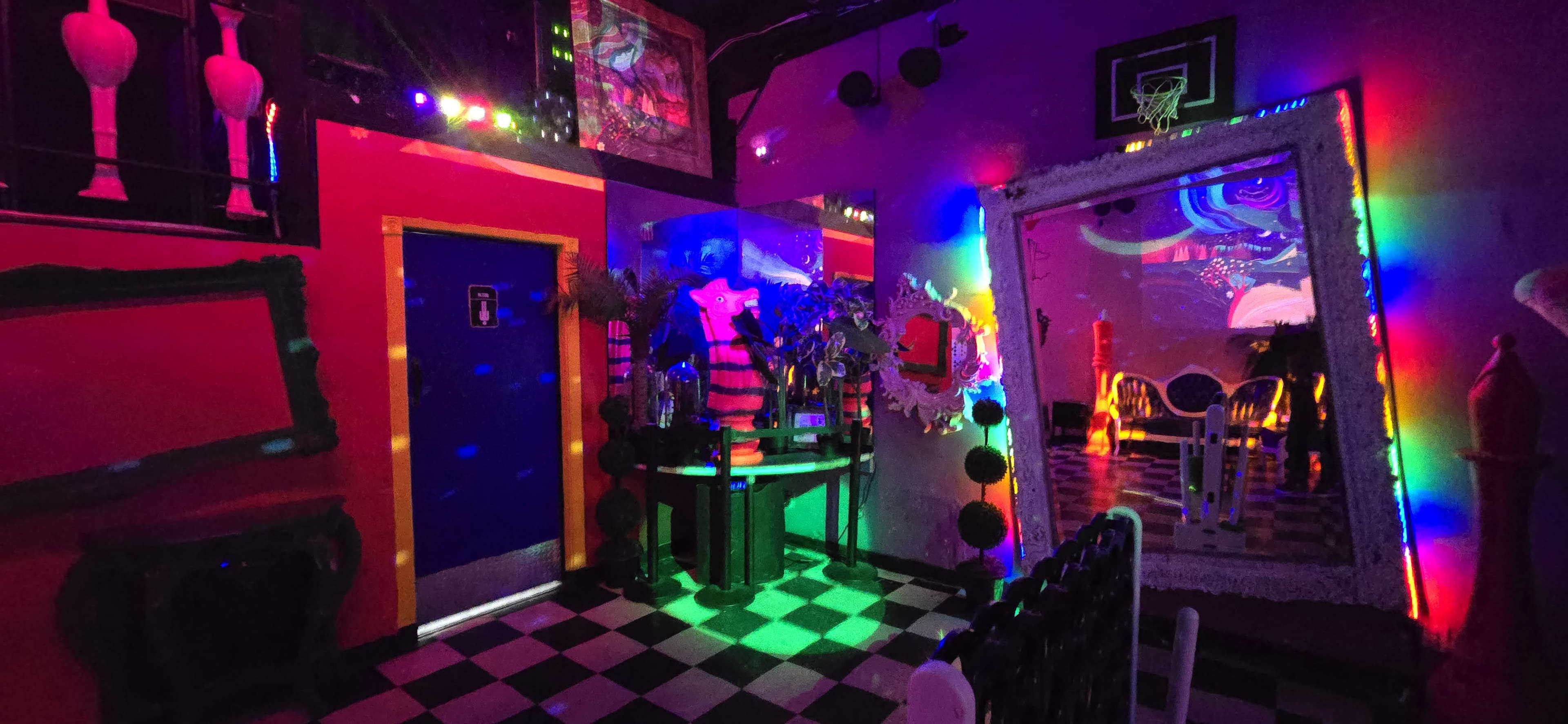 A vibrant room with multicolored lights, featuring a checkerboard floor, decorative mirrors, and various artistic elements on the walls.