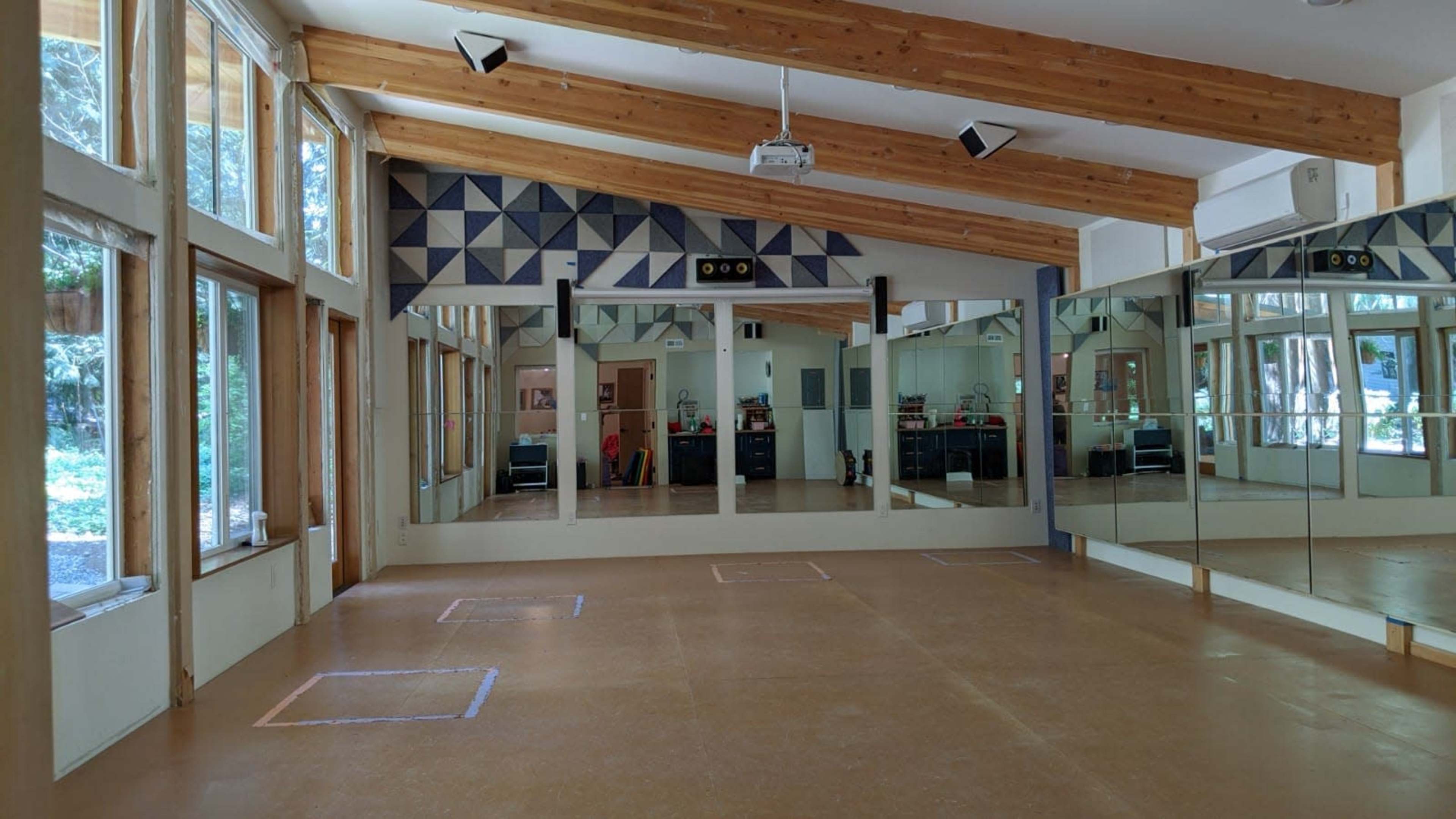 A spacious dance studio with large windows, wooden beams, and mirrored walls.