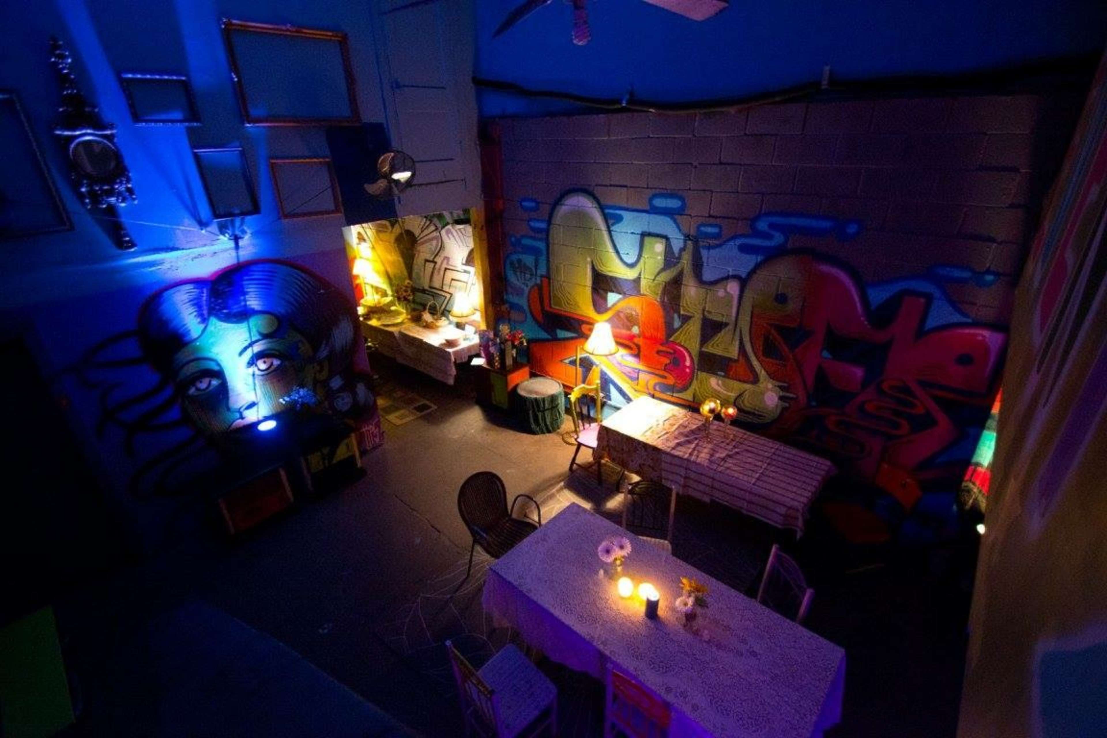 The image shows an indoor space with colorful graffiti on the walls and two tables set with candles and flowers under dim lighting.