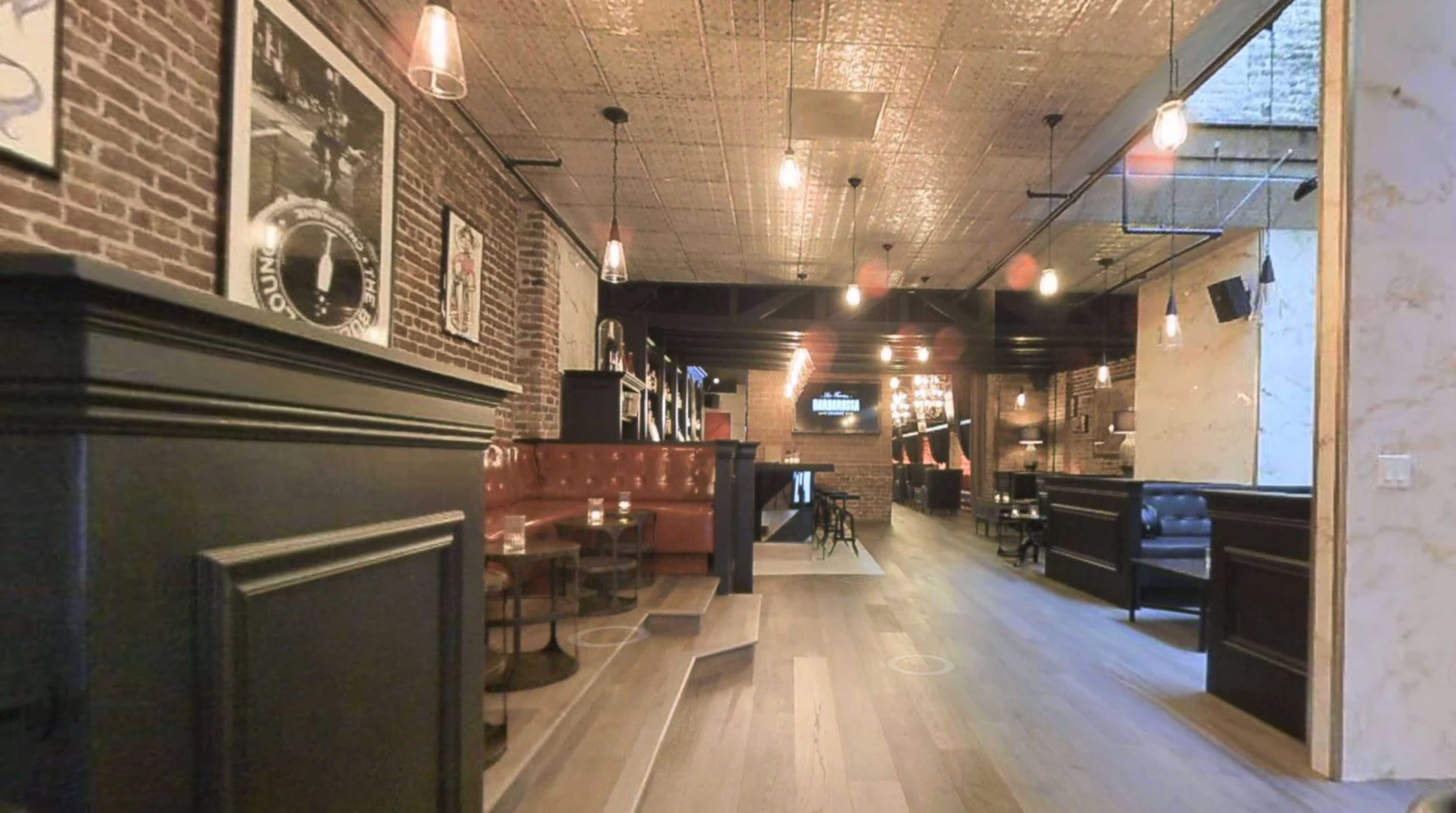 The image shows a stylish restaurant interior with exposed brick walls, wooden flooring, and a mix of booth and table seating under warm lighting.