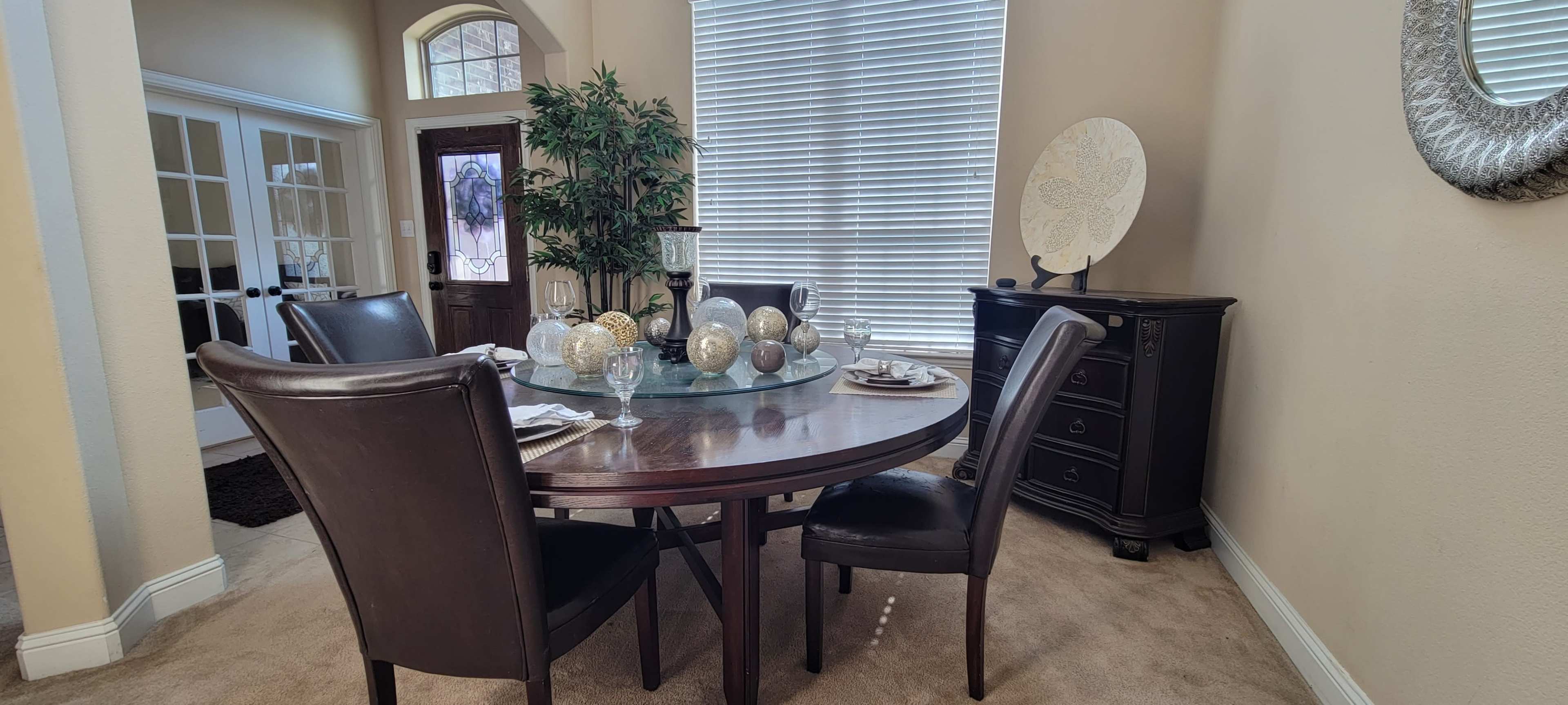 A dining area with a round wooden table set for a meal, surrounded by four black chairs, and decorated with spherical centerpieces and a side cabinet against the wall.