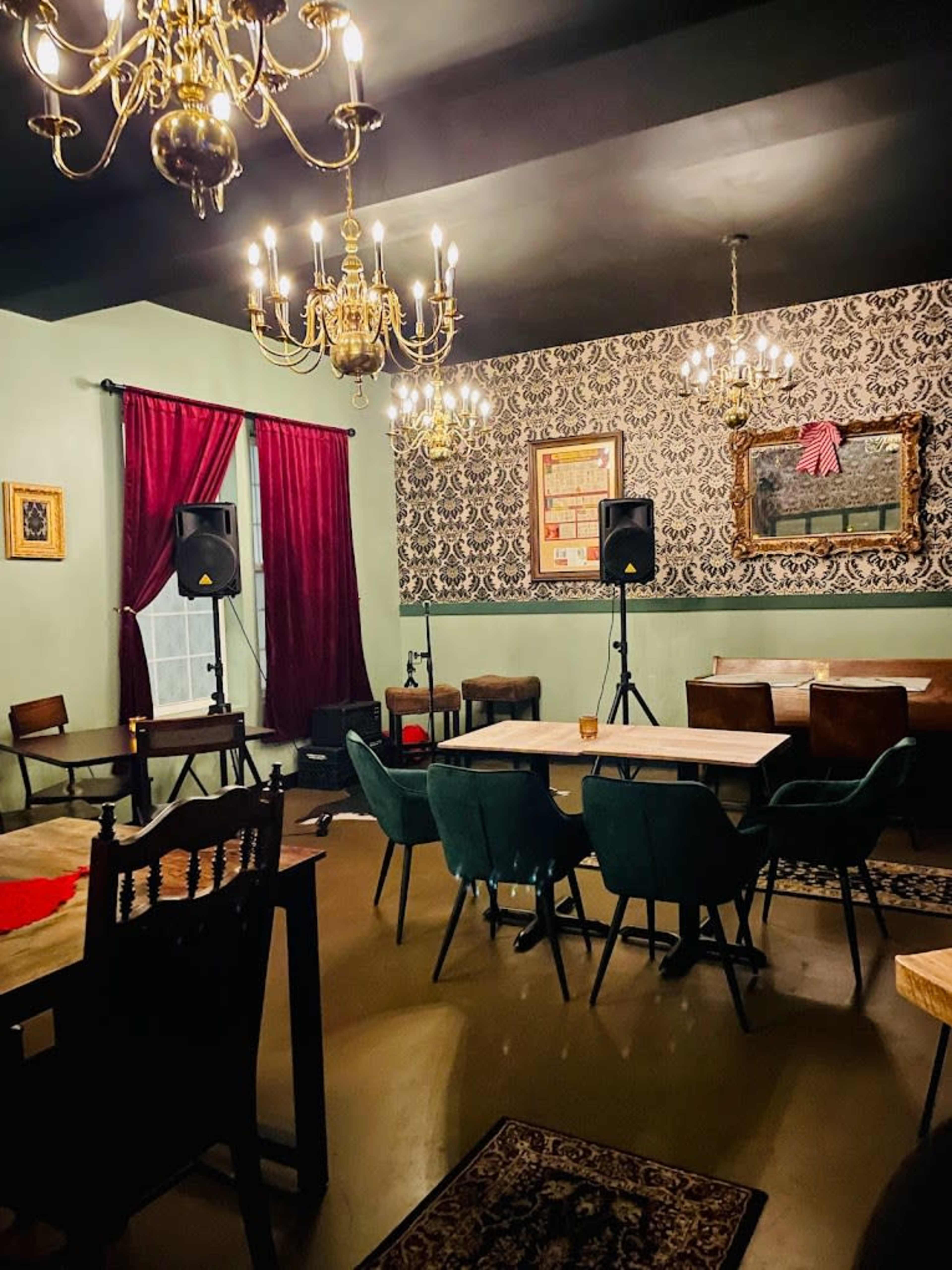The image shows a dimly lit lounge with chandeliers, dark velvet curtains, and a mix of tables and seating arranged around a patterned wall.