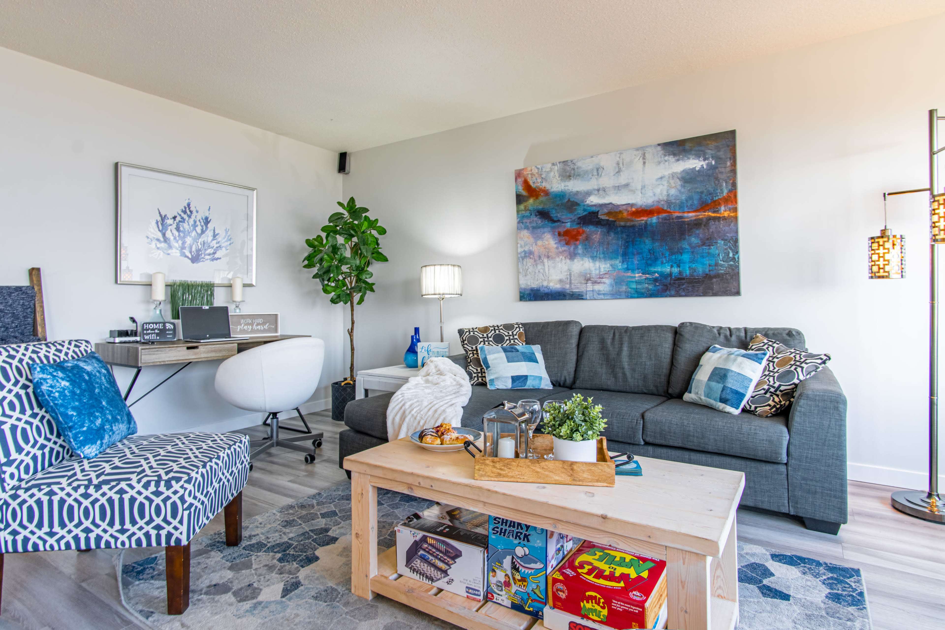 A modern living room with a gray sofa, a wooden coffee table displaying magazines, and a patterned armchair beside a small desk.
