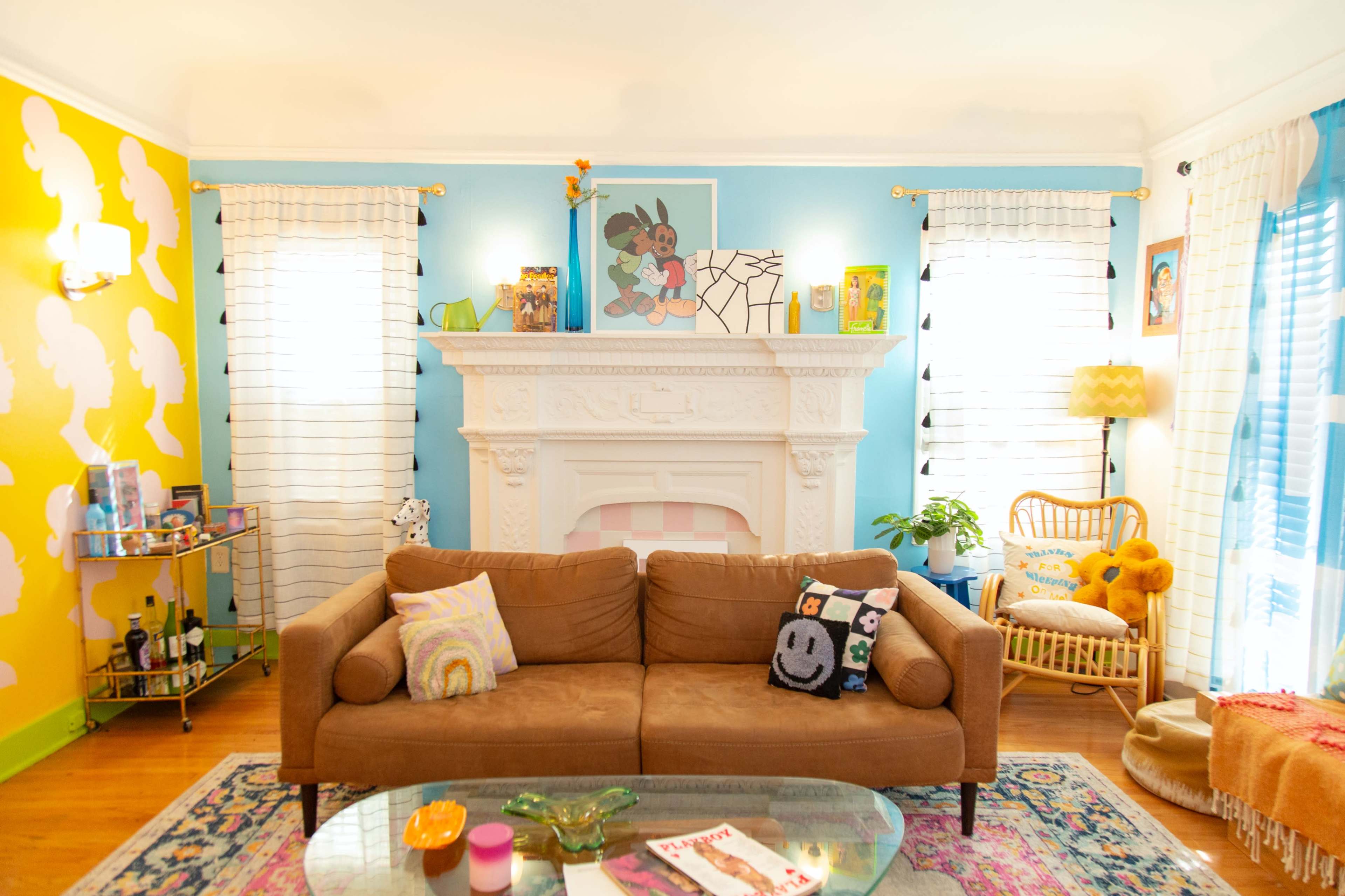 The image shows a brightly decorated living room with a brown sofa, colorful walls, a fireplace, and various decorative items.