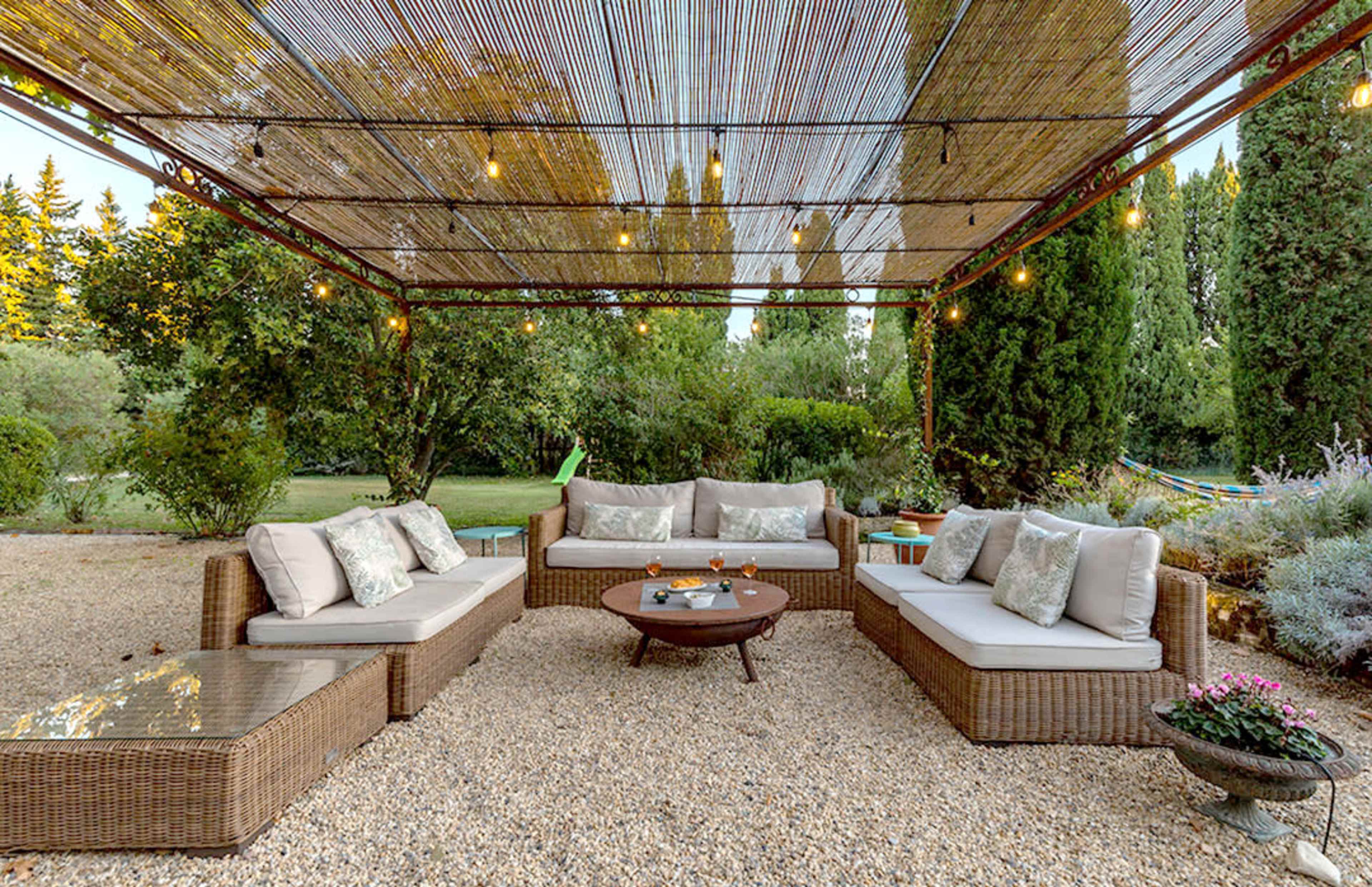 A patio area features a seating arrangement of wicker furniture with gray cushions around a circular table, under a bamboo canopy adorned with string lights.